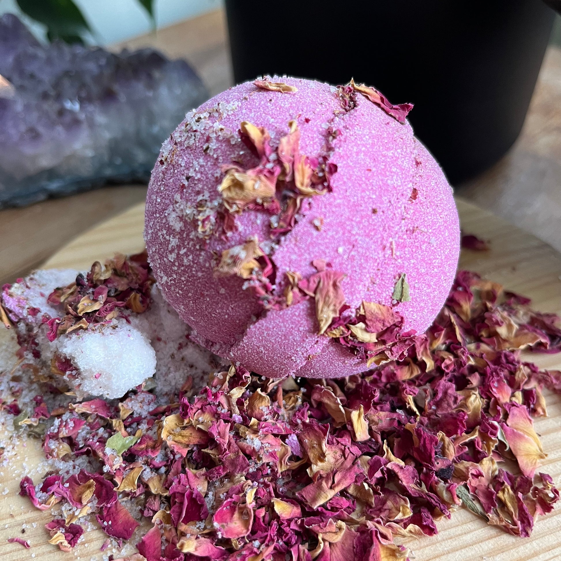 Pink bath bomb sitting on a bed of red rose petals and white himalayan salt