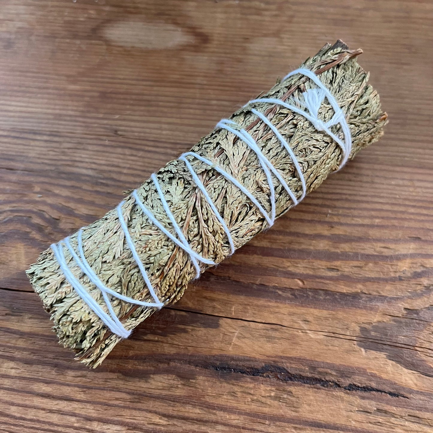 A rolled sage smudge bundle wrapped in white string, placed diagonally on a rustic wooden surface.