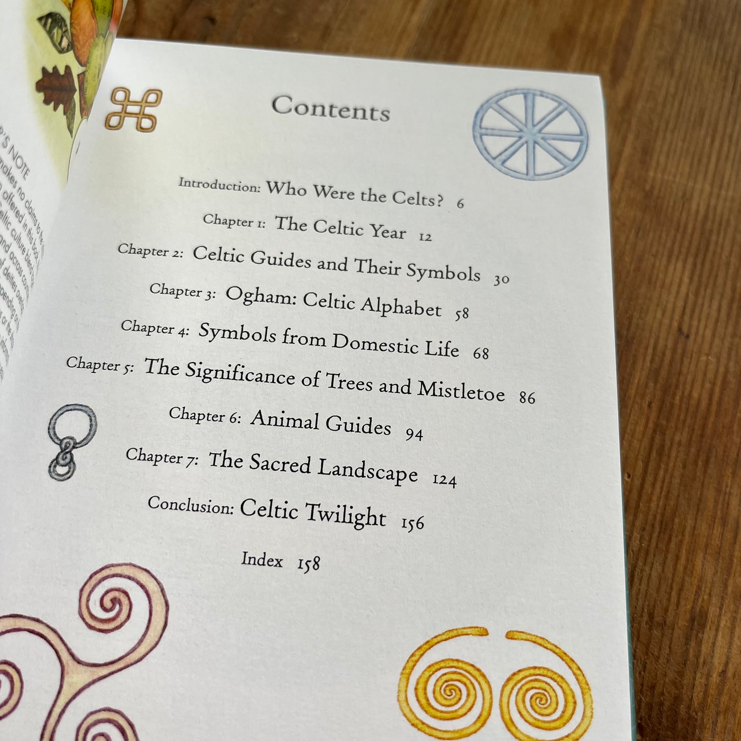 An open book showing a printed Contents page with chapter titles and decorative Celtic-style symbols, photographed on a wooden surface.