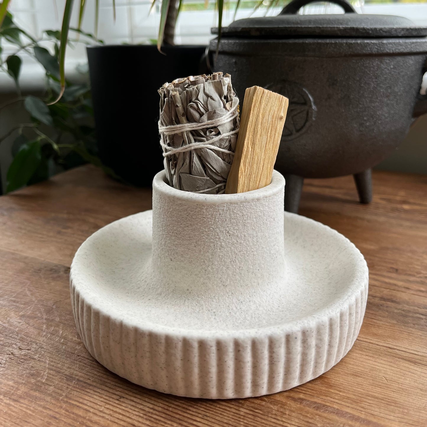 White ceramic holder with incense sticks and a wrapped sage bundle on a wooden surface.