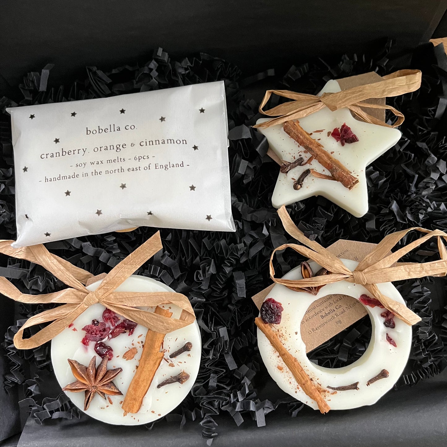 Three festive shaped hanging wax melt decorations and a pack of mini wax melts n a gift box, on a wooden surface.