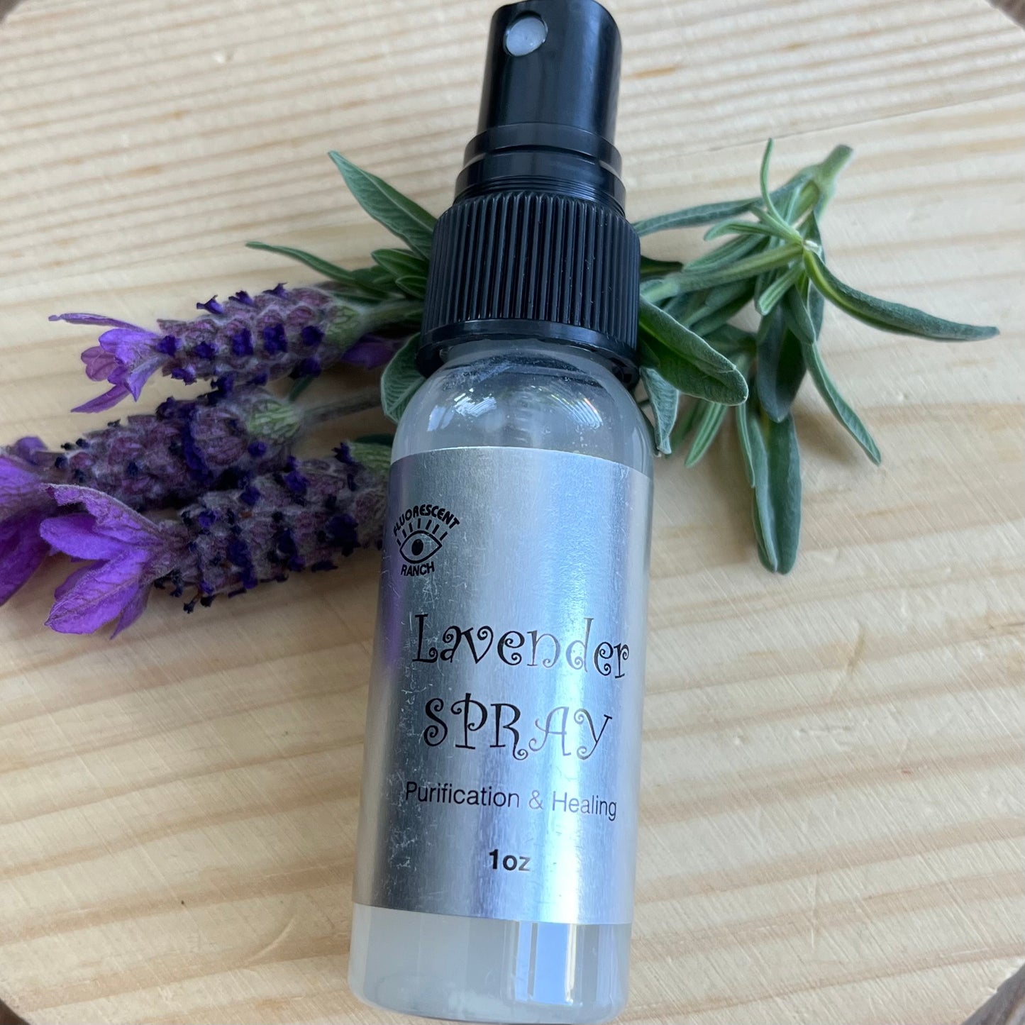 Lavender room spray in a clear glass spray bottle pictured with a sprig of Lavender