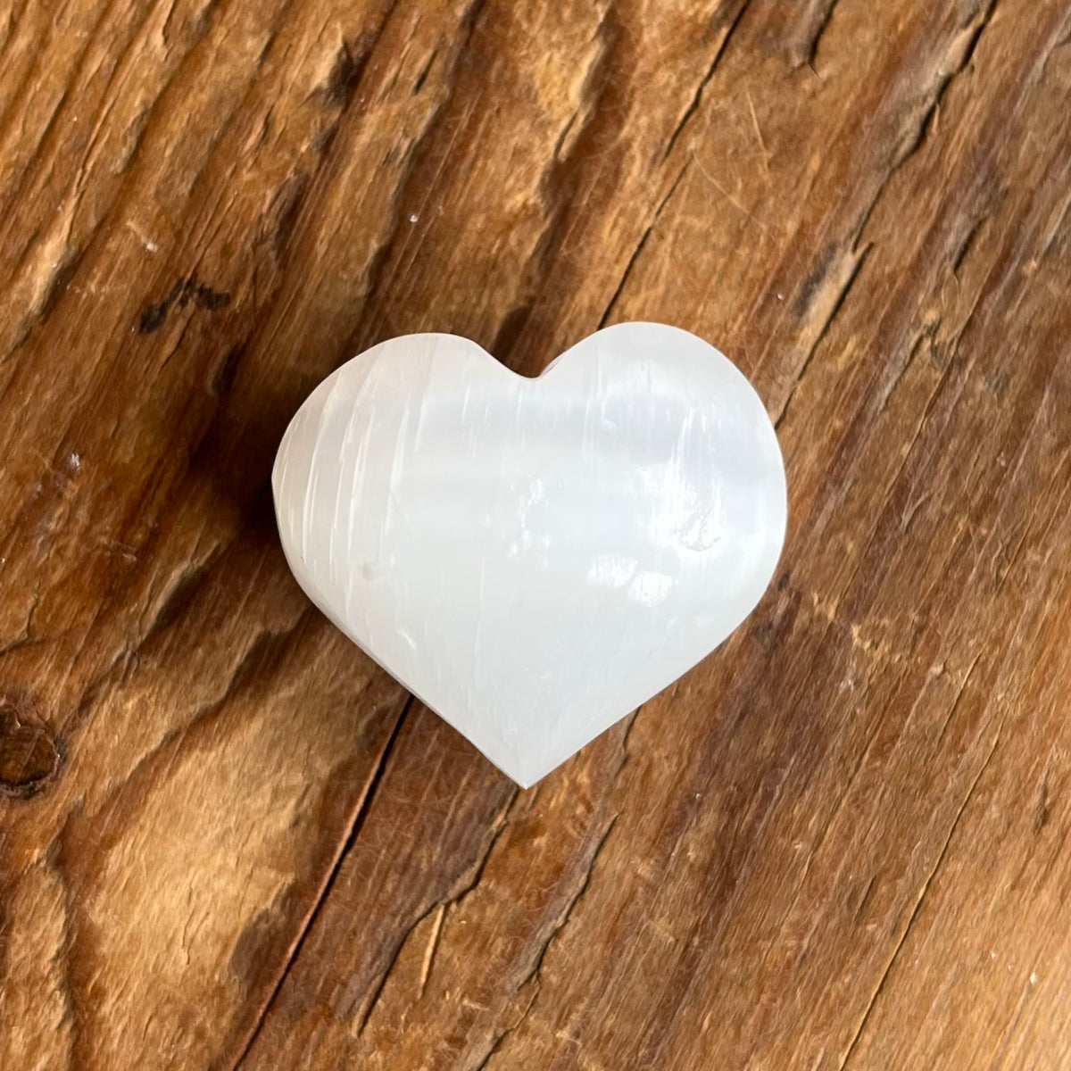 A polished white heart-shaped stone, likely selenite, resting on a rustic brown wooden surface.