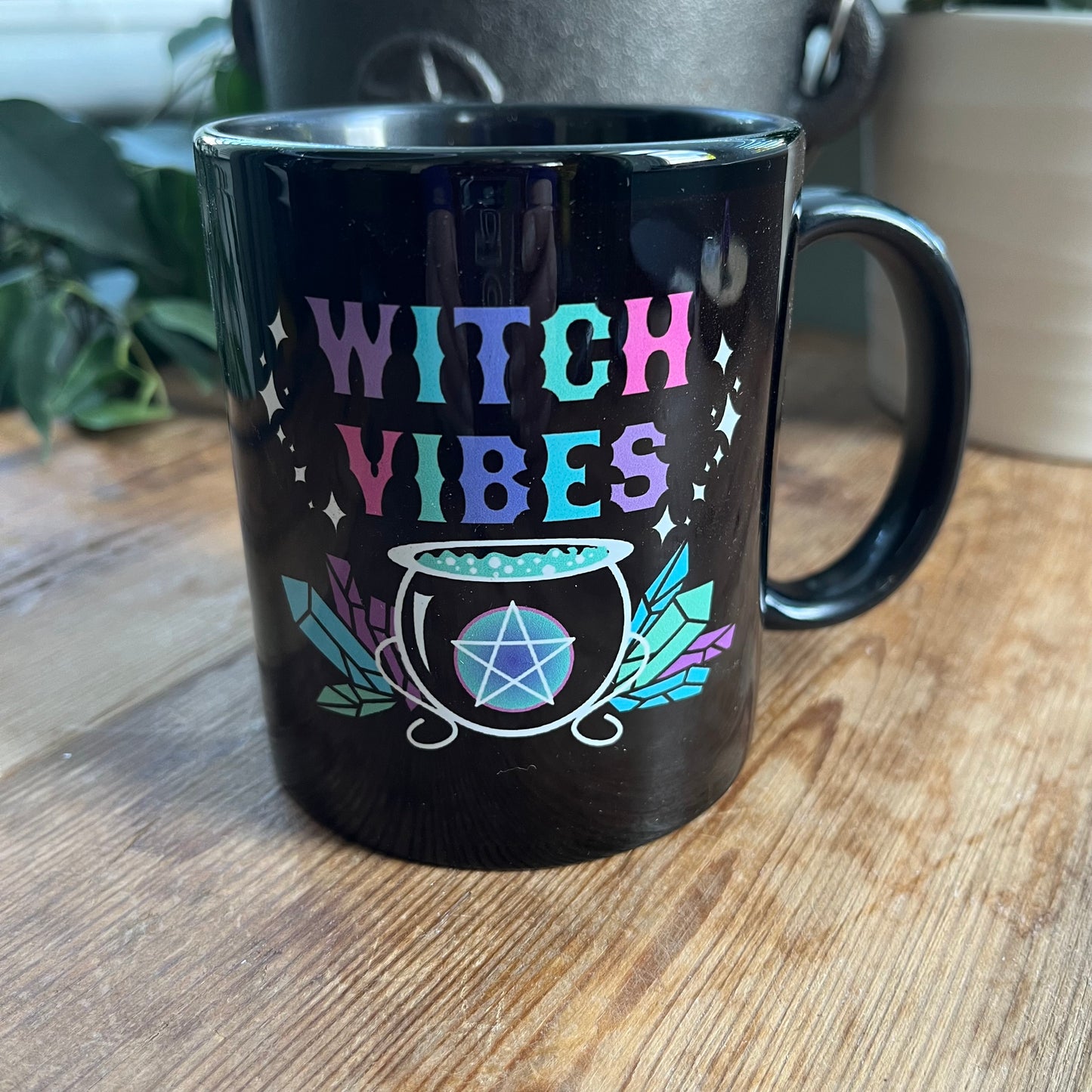 Black mug with the words witch vibes in colourful text and an illustration of a cauldron , crystals and pentagram