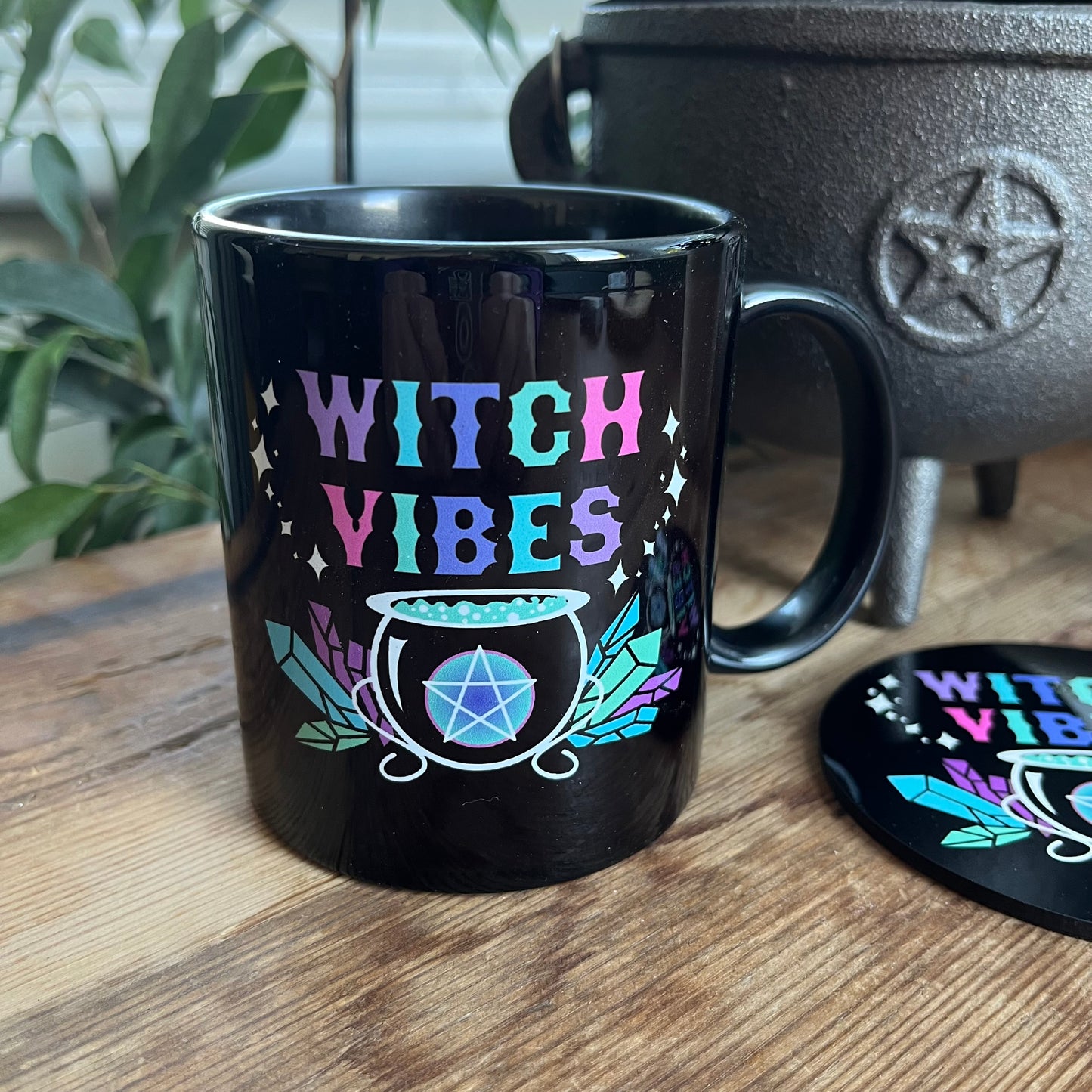Black mug with the words witch vibes in colourful text and an illustration of a cauldron , crystals and pentagram