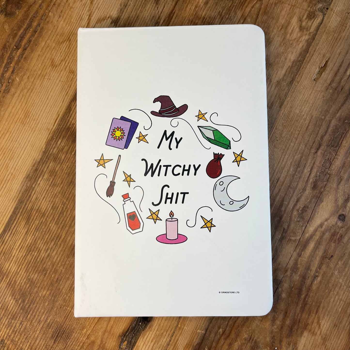 A cream A5 notebook with withy symbols and the words ;my witchy shit' on the cover