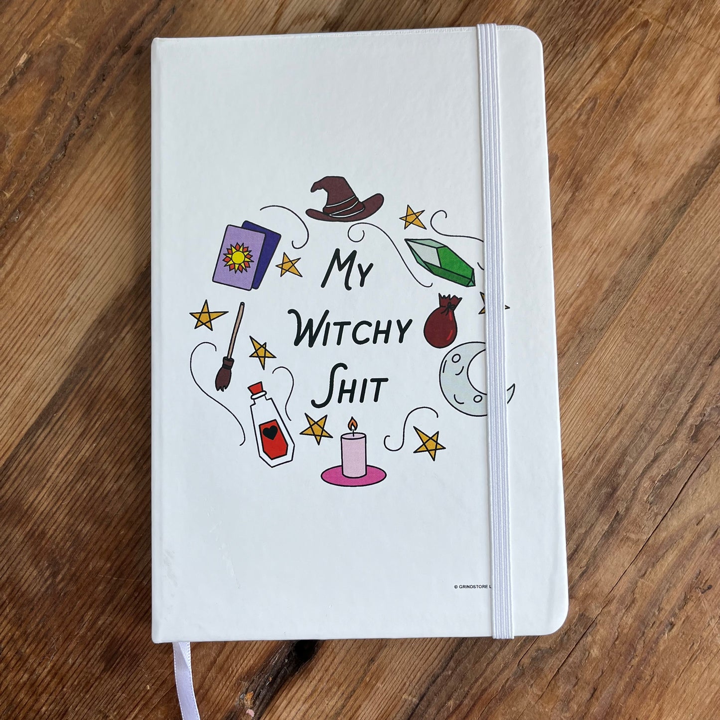 A cream A5 notebook with withy symbols and the words ;my witchy shit' on the cover