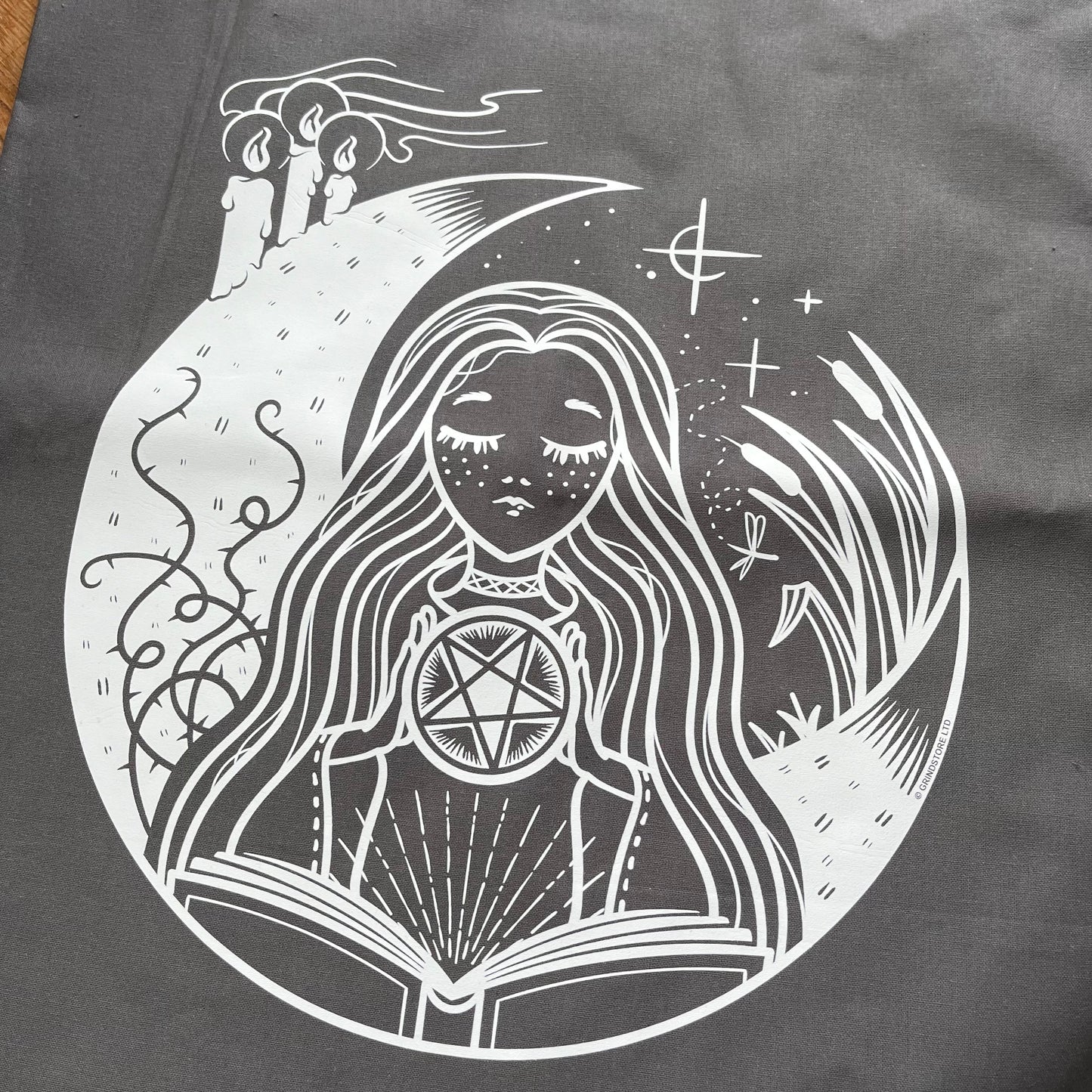 Black and white illustration of a woman with long hair, wearing a pentagram necklace, surrounded by nature elements on a dark background.