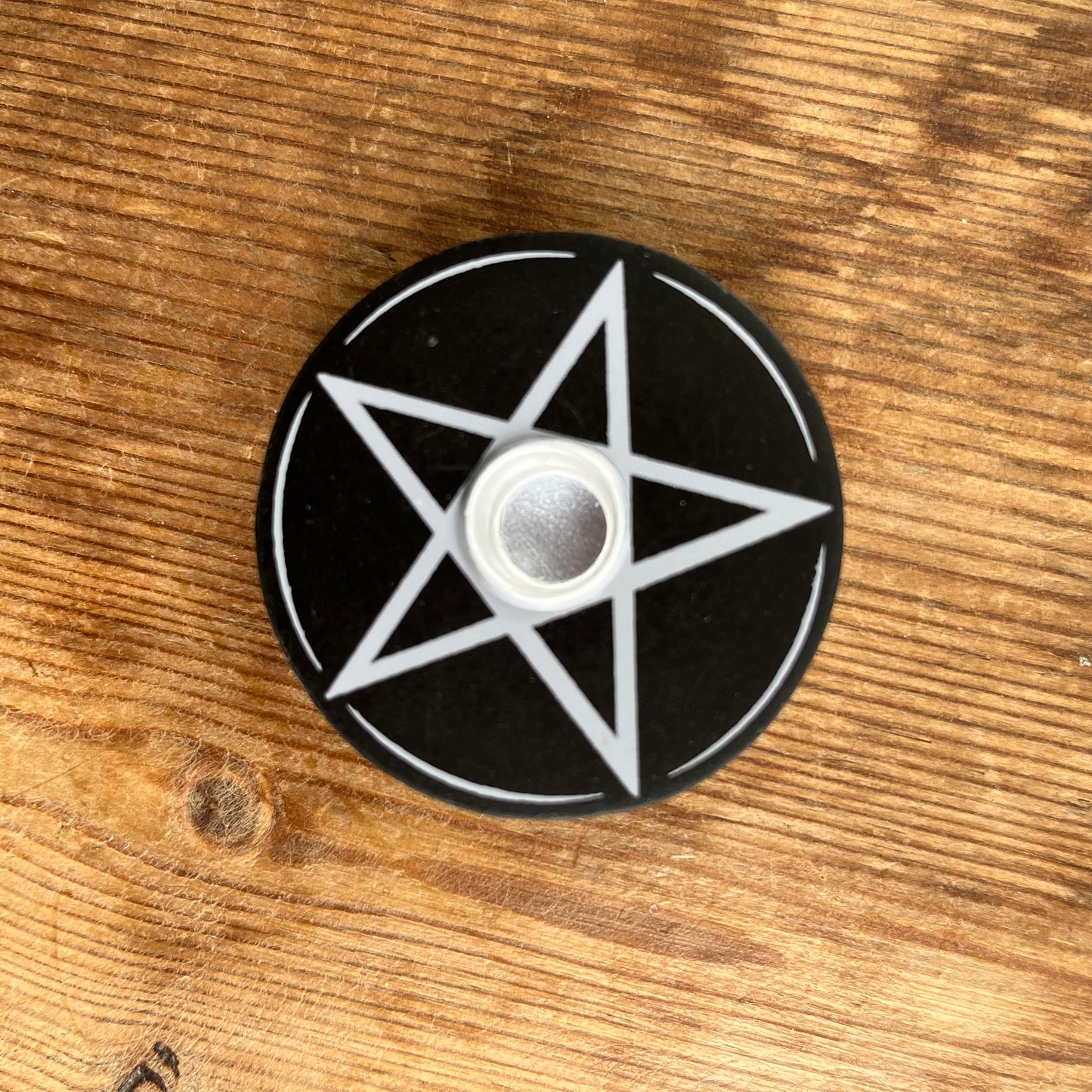 Circular black wooden candle holder with a white pentagram design on its surface designed to hold spell candles.