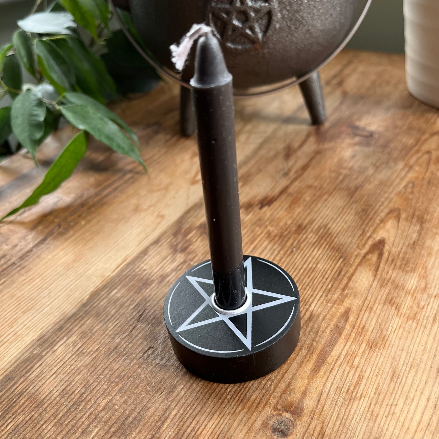 Circular black wooden candle holder with a white pentagram design on its surface designed to hold spell candles. holding a black spell candle