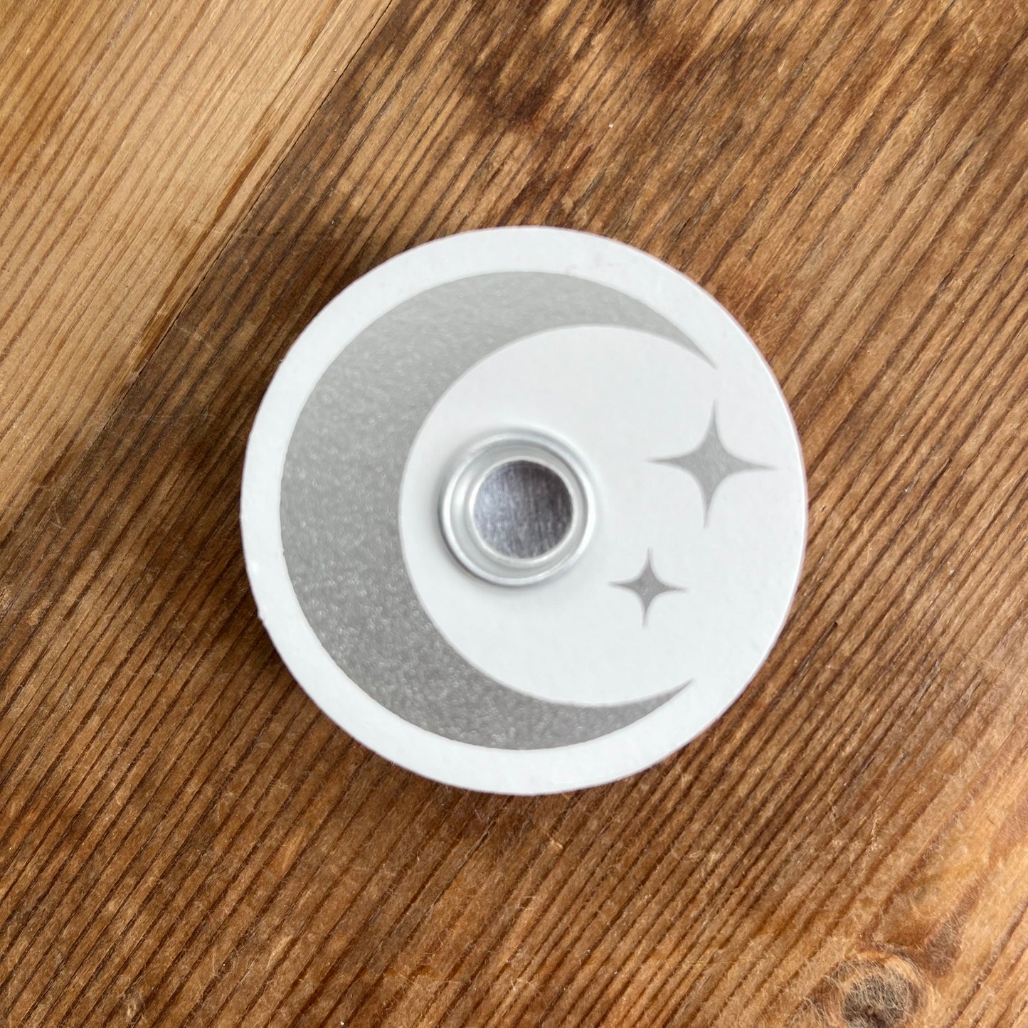 White circular wooden candle spell holder with a silver moon and star design on its surface
