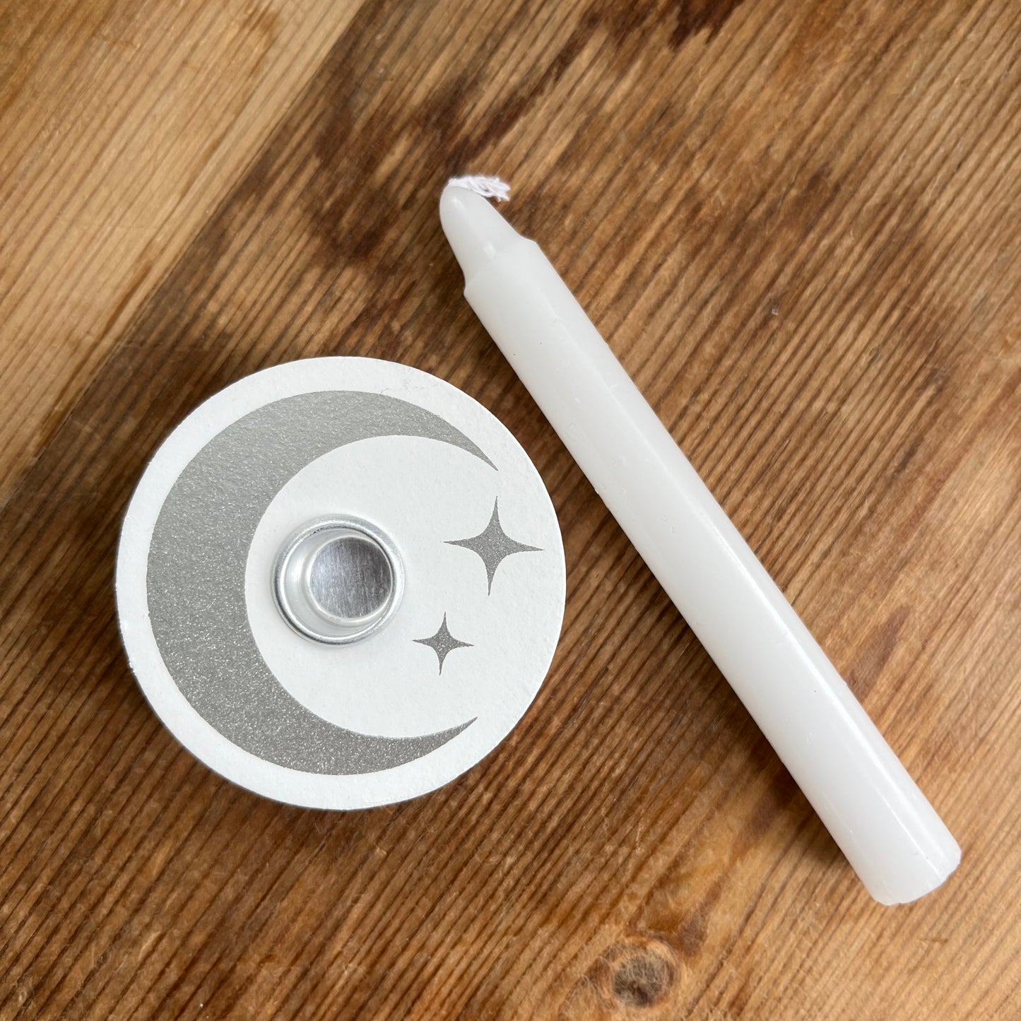 White circular wooden candle spell holder with a silver moon and star design on its surface