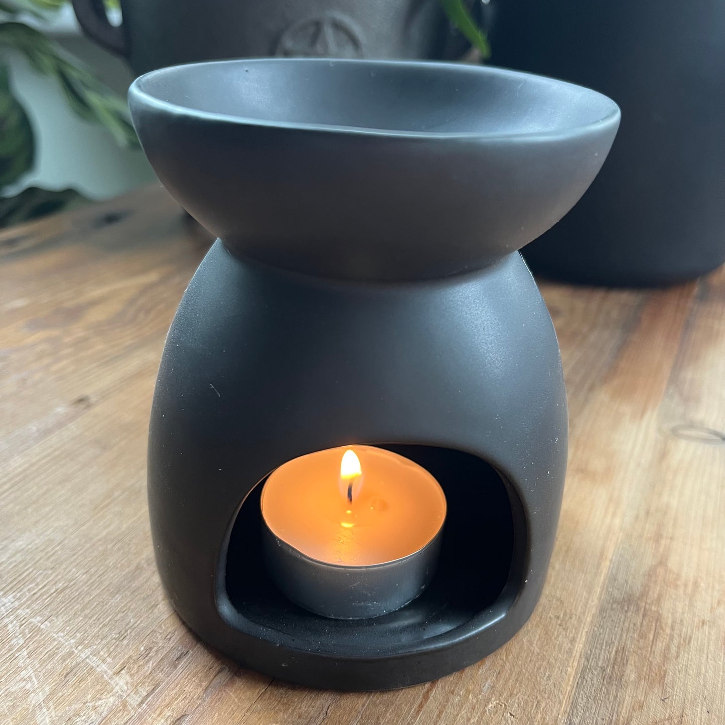 Black ceramic oil burner, featuring a pentagram cutout design and a smooth matte finish. Pictures the back with a tealight inserted