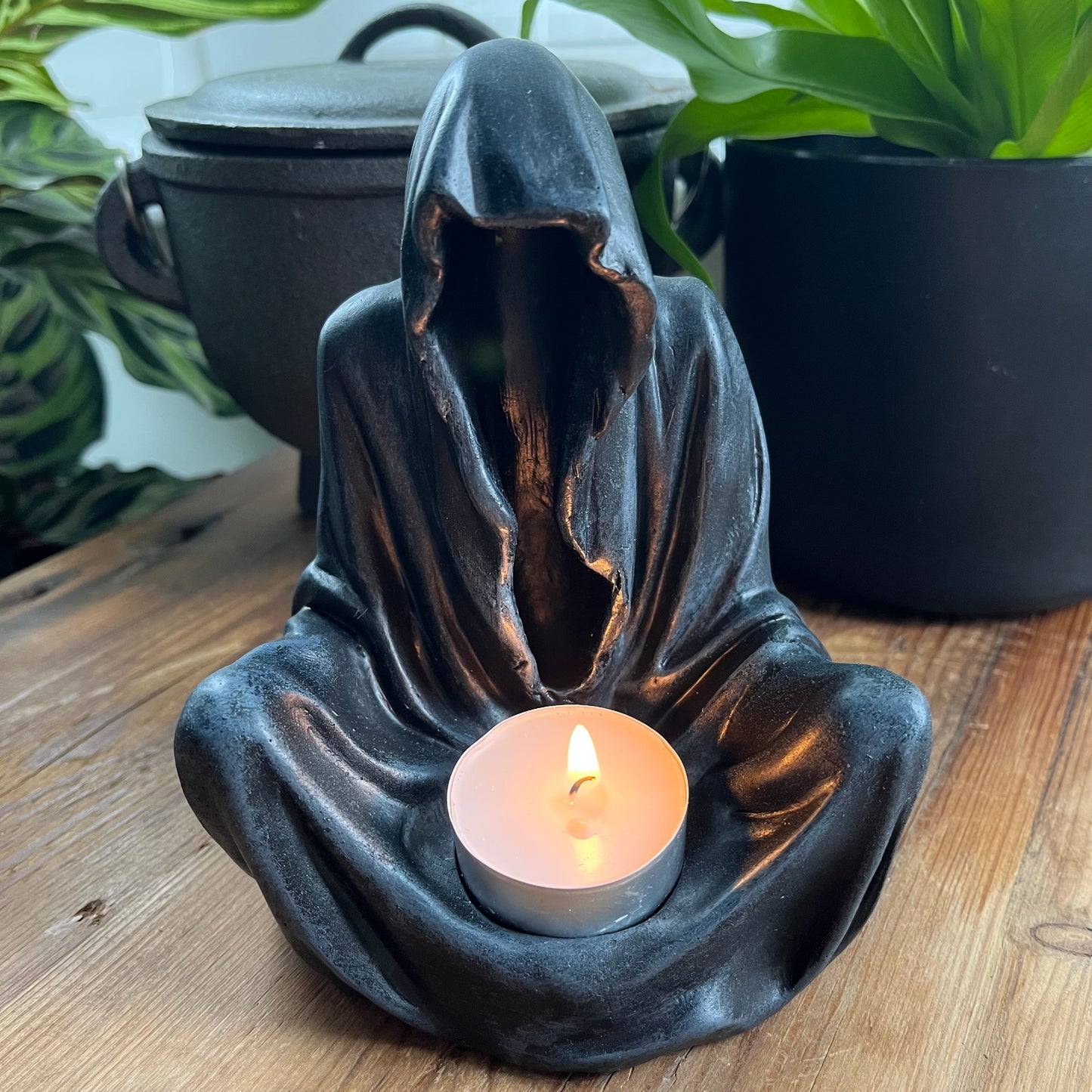 A Goth grim reaper looking, black-veiled figure sits holds a tealight in its lap to create a mysterious, magical light.