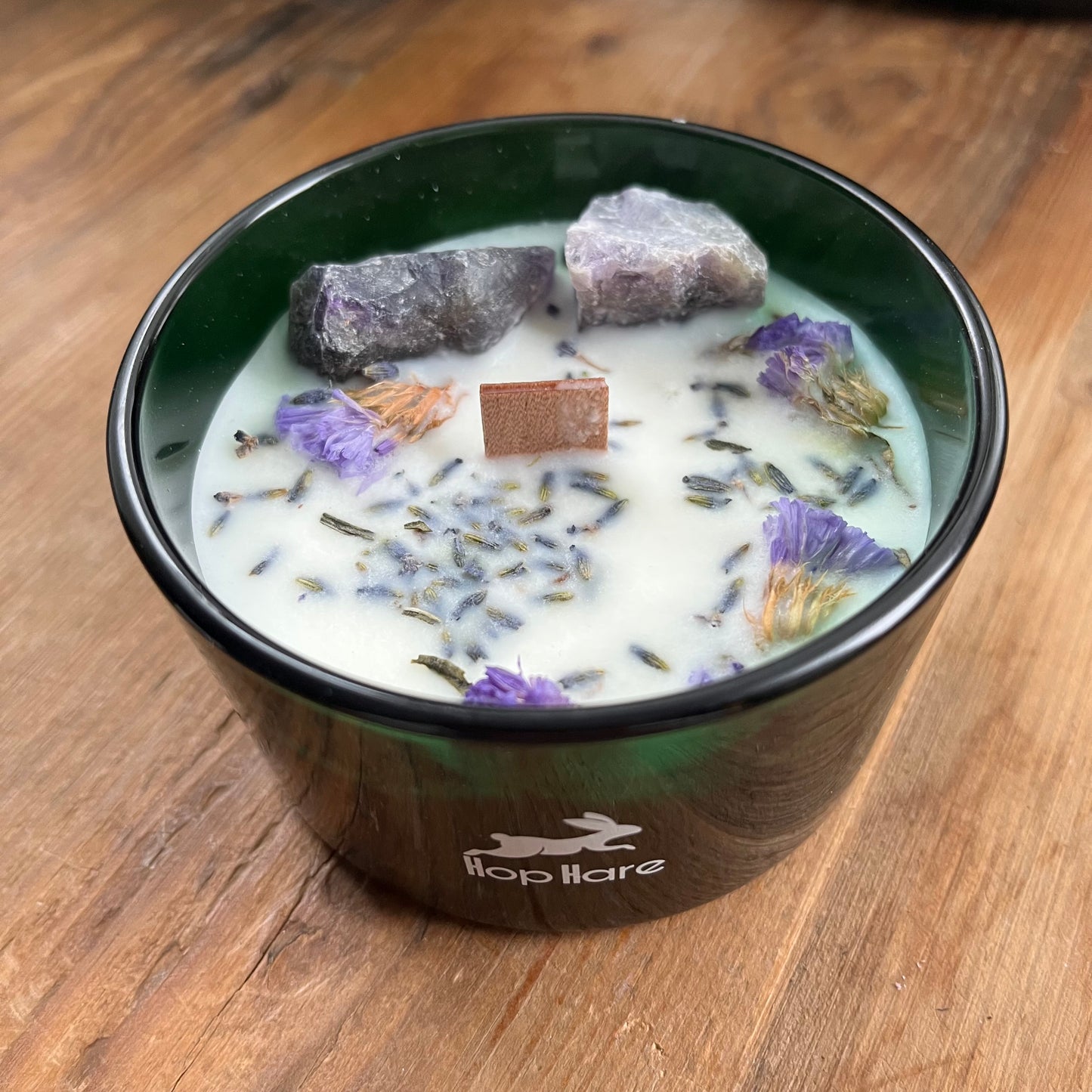The top of the hop hare moon candle shows a wooden wick, large amethyst crystals and lavender flowers