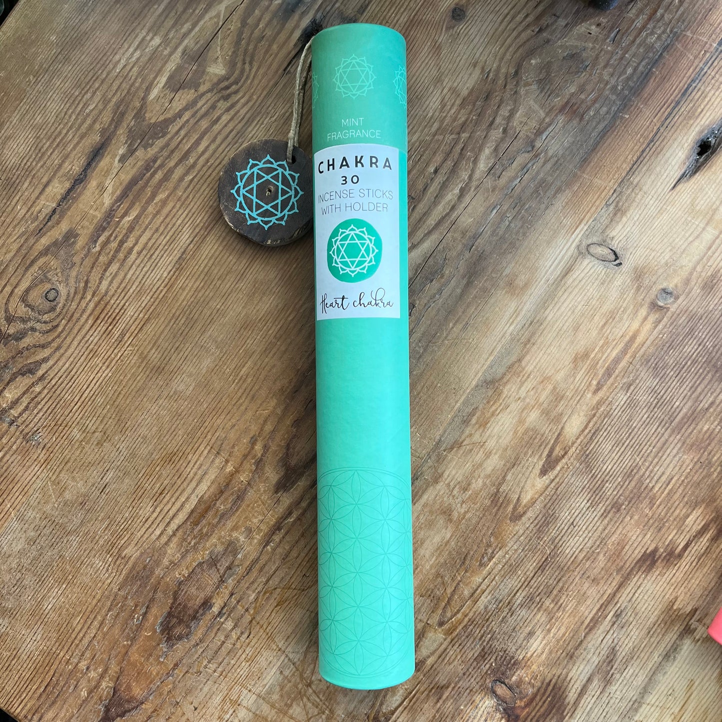 Green cardboard tube containg 30 sticks of mint scented incense for the Heart Chakra, with a wooden incense holder printed with the symbol for the Heart Chakra