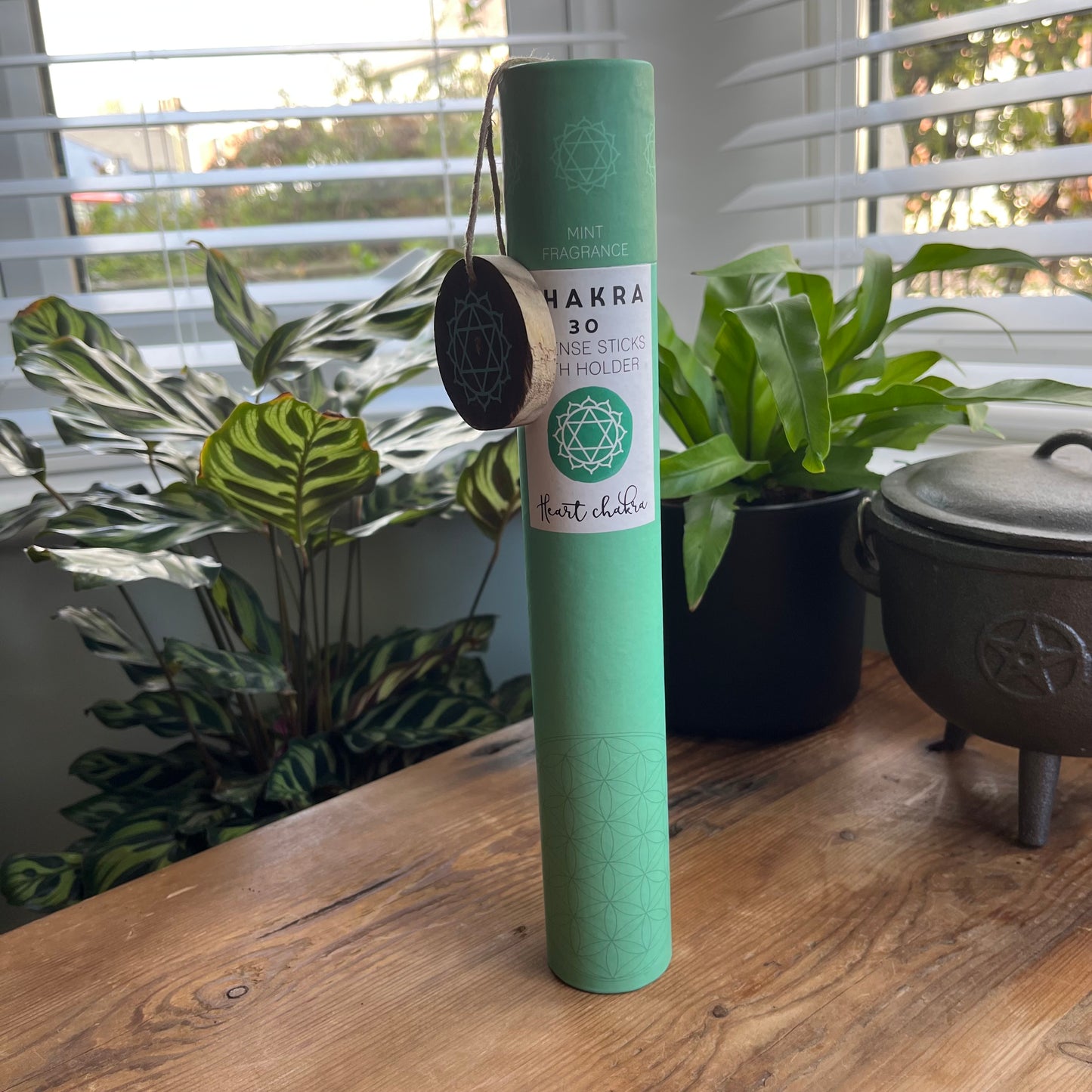 Green cardboard tube containg 30 sticks of mint scented incense for the Heart Chakra, with a wooden incense holder printed with the symbol for the Heart Chakra