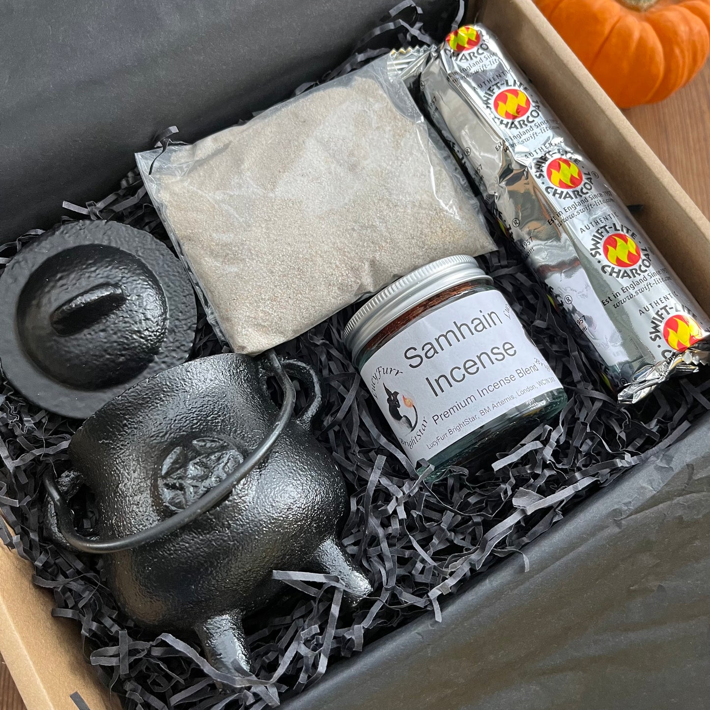 Box containing Samhain Incense, a small black cauldron, and other items on a wooden surface.