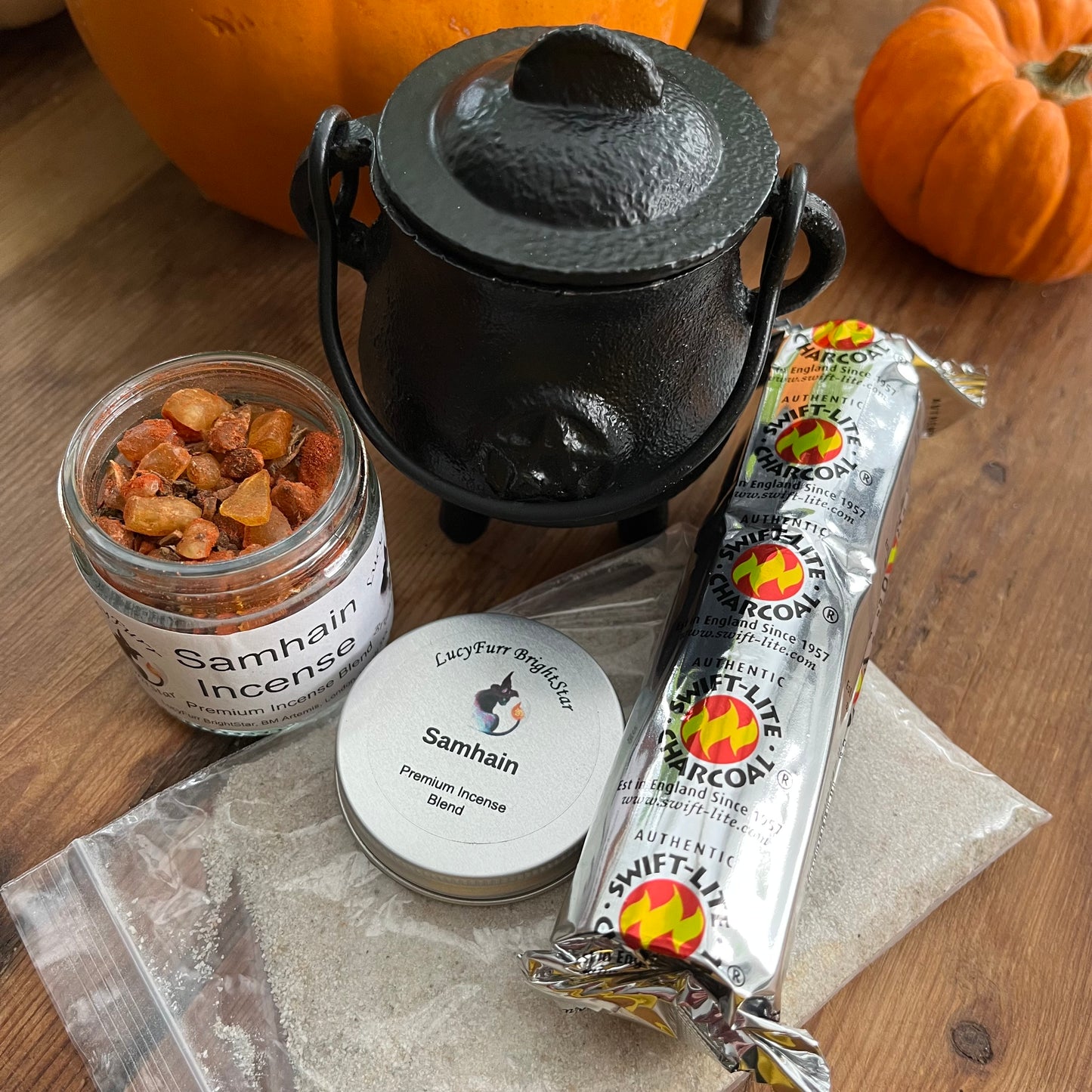 Incense products including a jar, black cauldron, and packets on a wooden surface with pumpkins in the background.