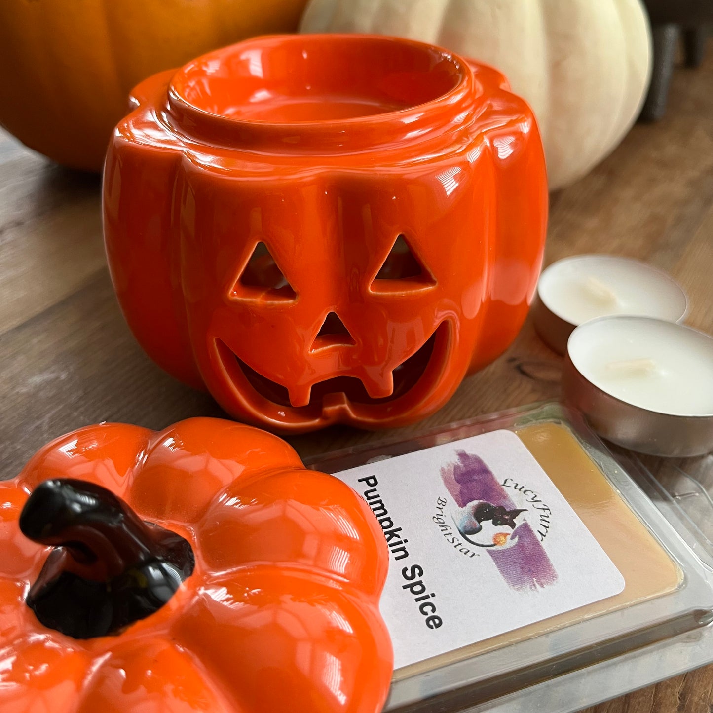 Orange pumpkin-shaped wax warmer with a lit candle on a wooden surface.