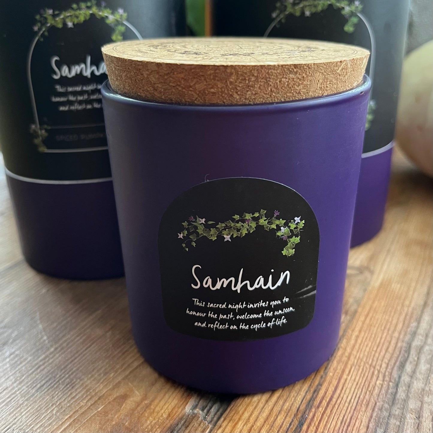 Purple container candle with cork lid and 'Samhain' label on a wooden surface