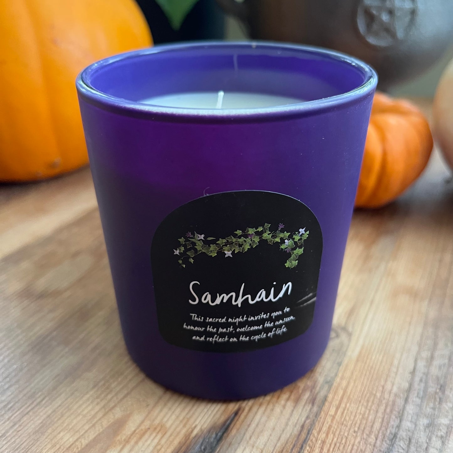 Purple candle with a Samhain label on a wooden surface with pumpkins in the background