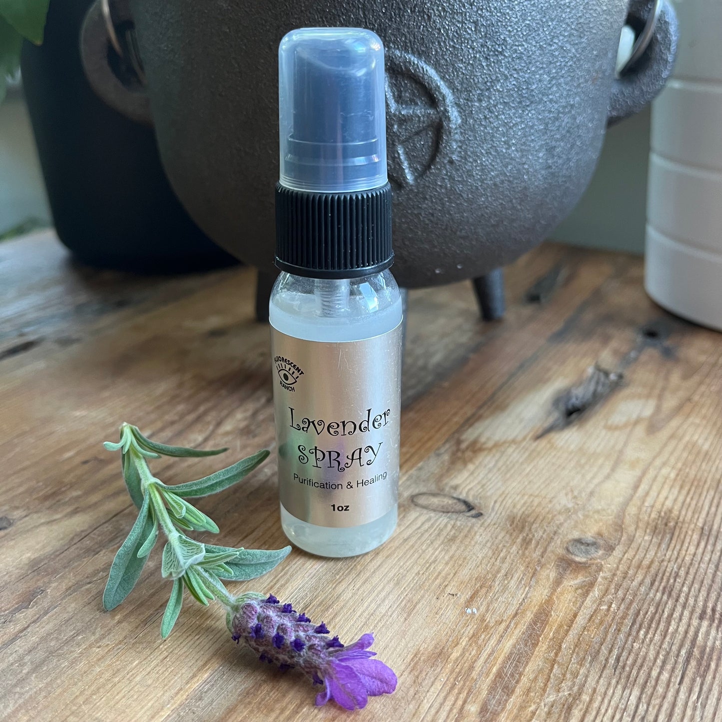 Lavender room spray in a clear glass spray bottle pictured with a sprig of Lavender