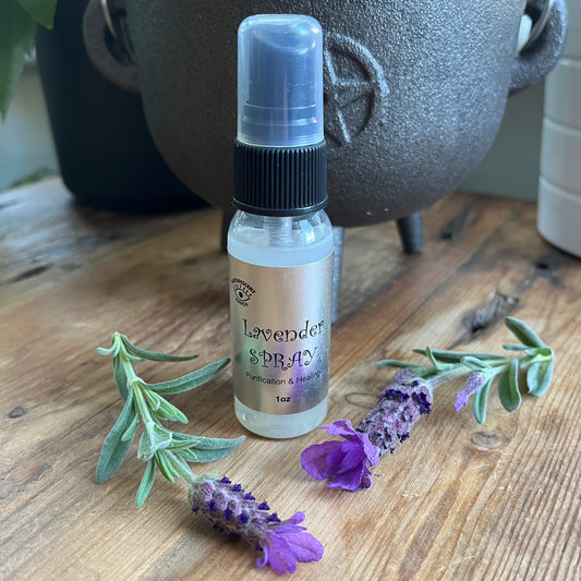Lavender room spray in a clear glass spray bottle pictured with a sprig of Lavender