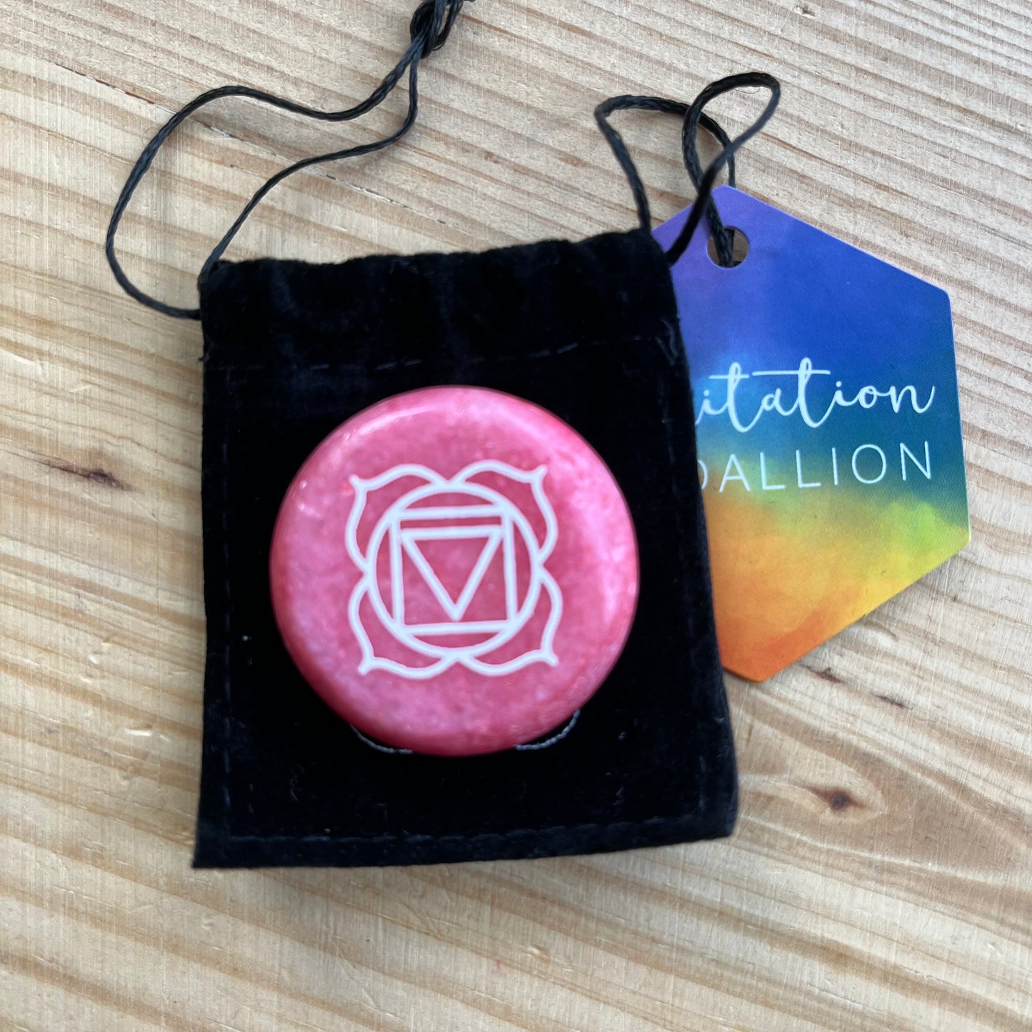A red circular flat meditation stone with the root chakra symbol on it, with a black velvet pouch.