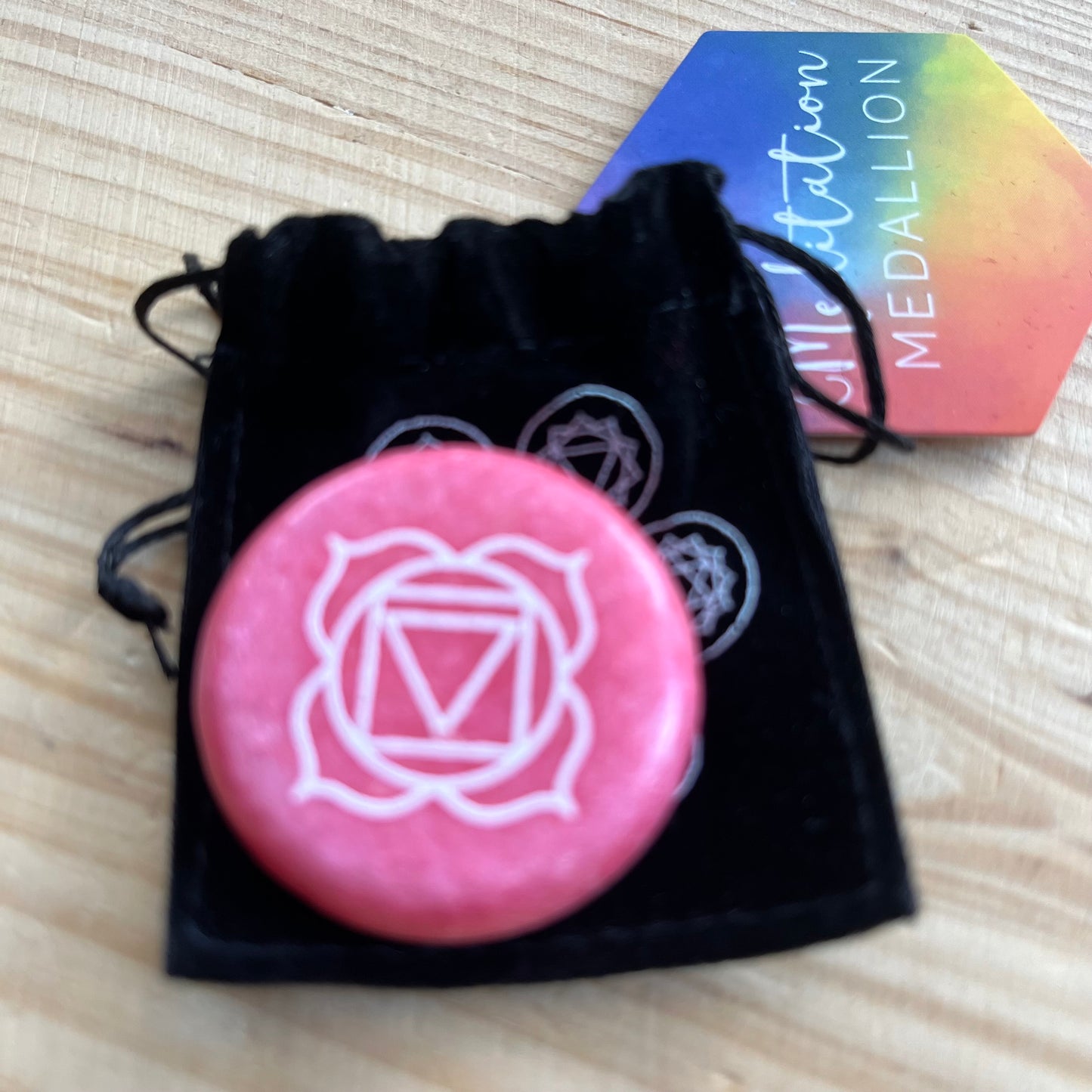 A red circular flat meditation stone with the root chakra symbol on it, with a black velvet pouch which has the 7 chakra smbols on it