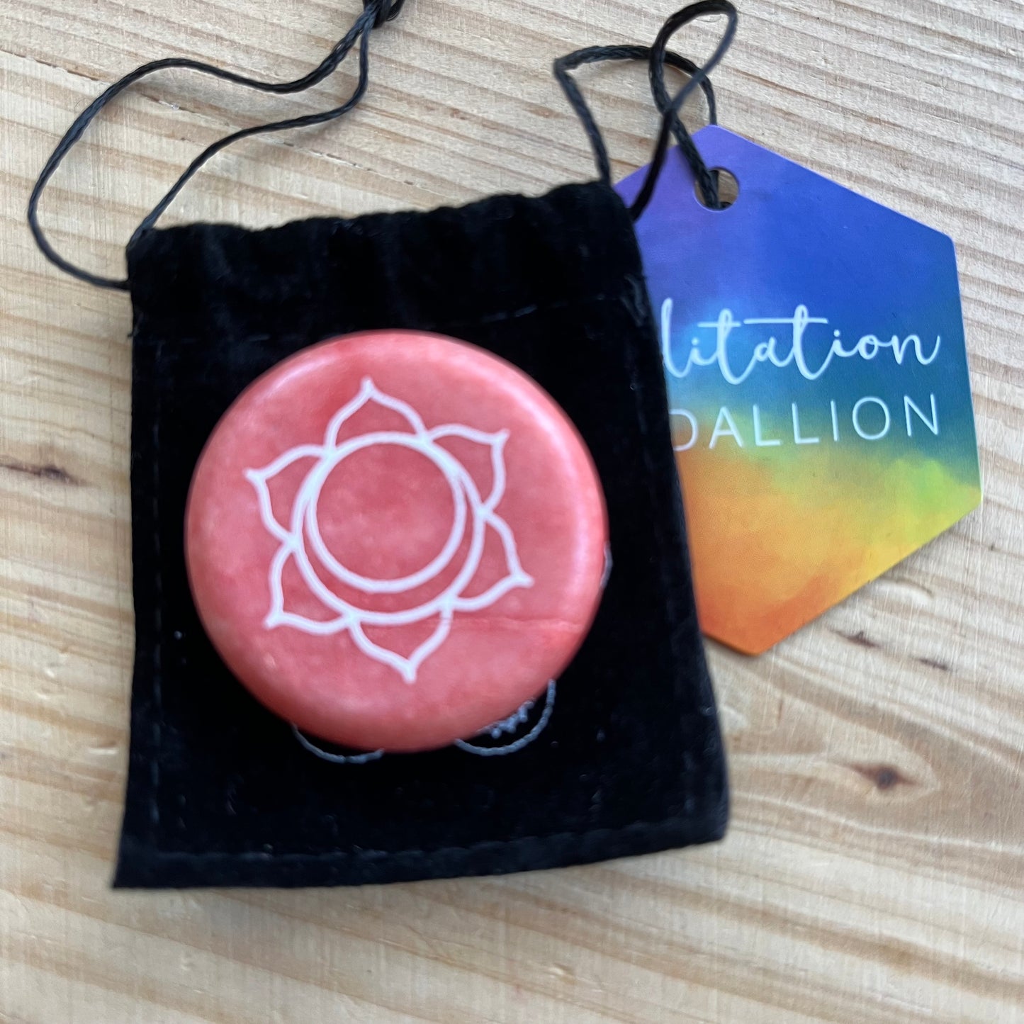 colourful circular flat meditation stone engraved with the Sacral Chakra symbol, alongside it's black velvet pouch