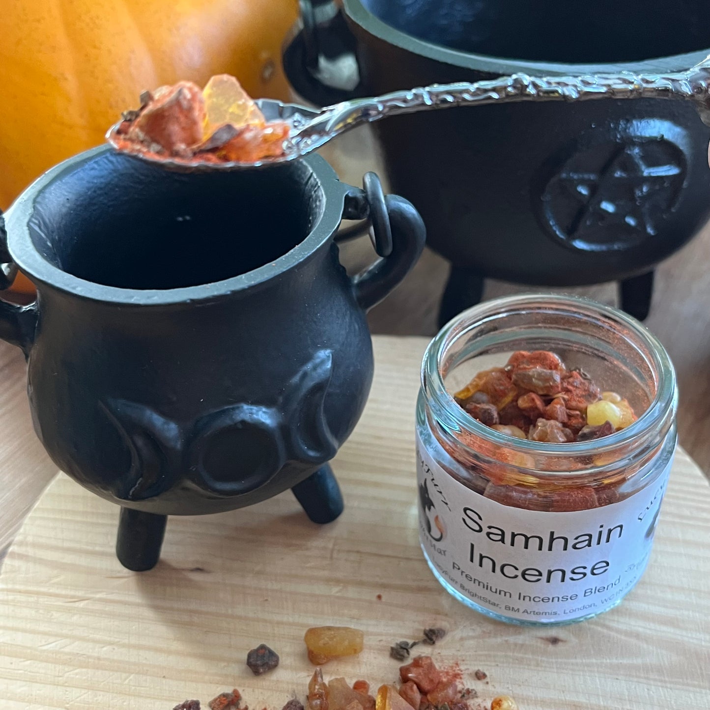 Black cauldron with Samhain incense and a jar of Samhain incense on a wooden surface.