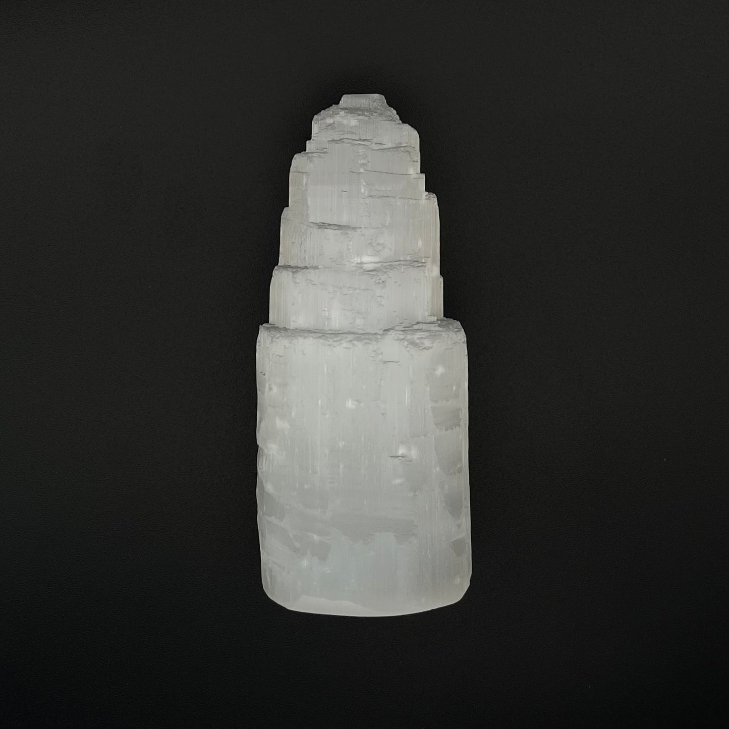 A natural white selenite tower crystal, showing layered, stacked geometric formations, photographed against a solid black background.