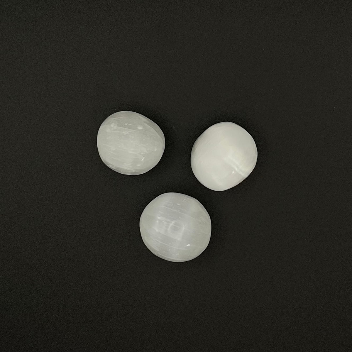 Three smooth, polished white stone beads arranged in a triangle on a dark black background.