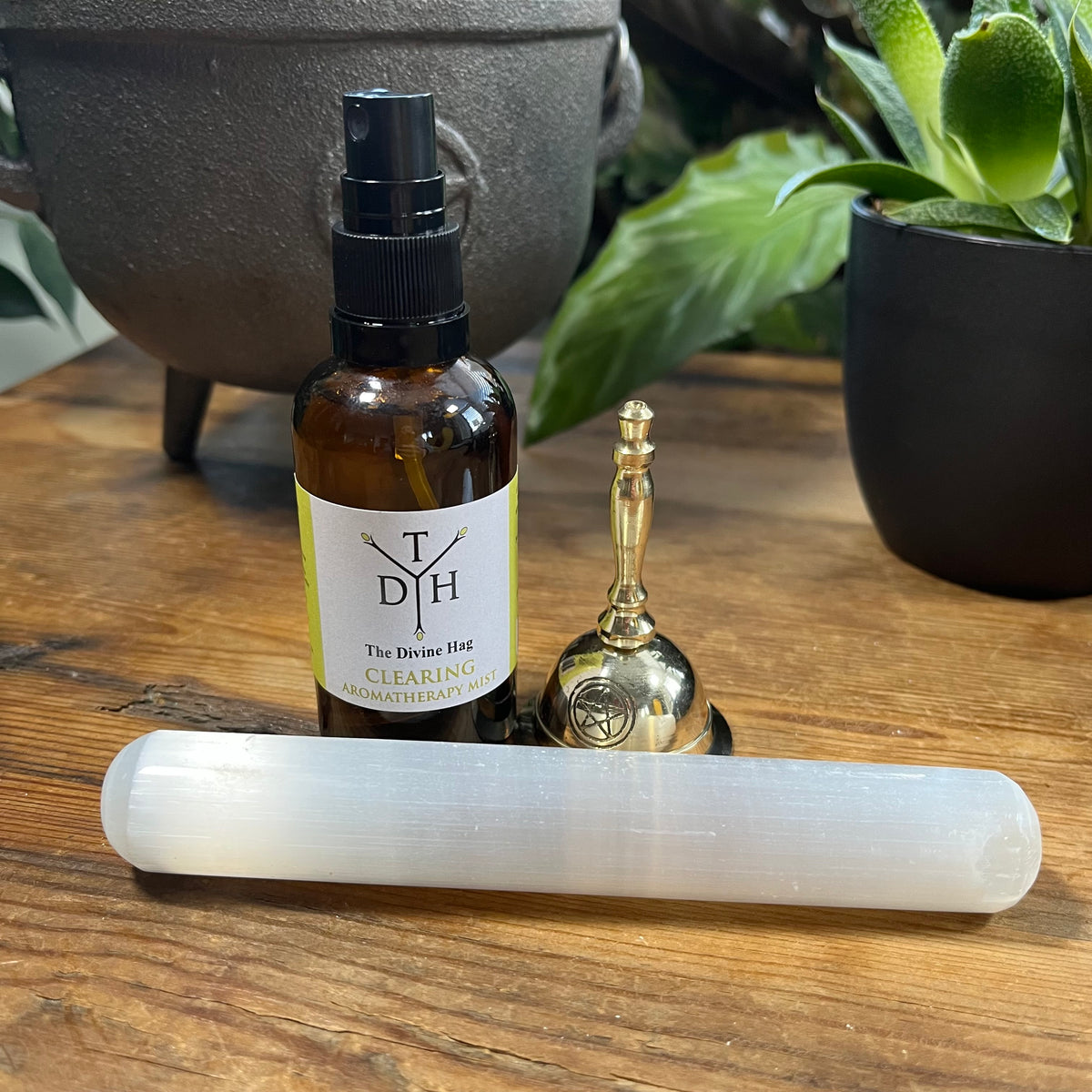 Bottle labeled 'TDH' Clearing Spray with a selenite crystal and bell on a wooden surface.