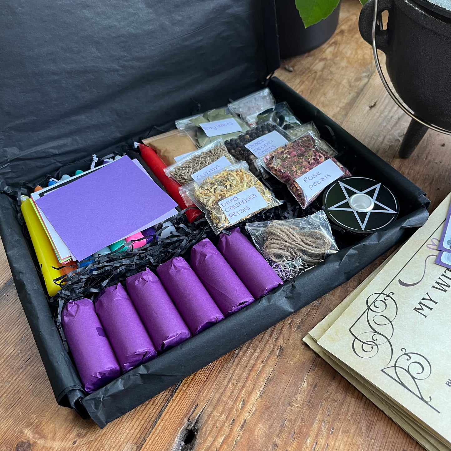 Witchcraft supplies including purple candles, herbs, and a pentacle symbol on a wooden surface.