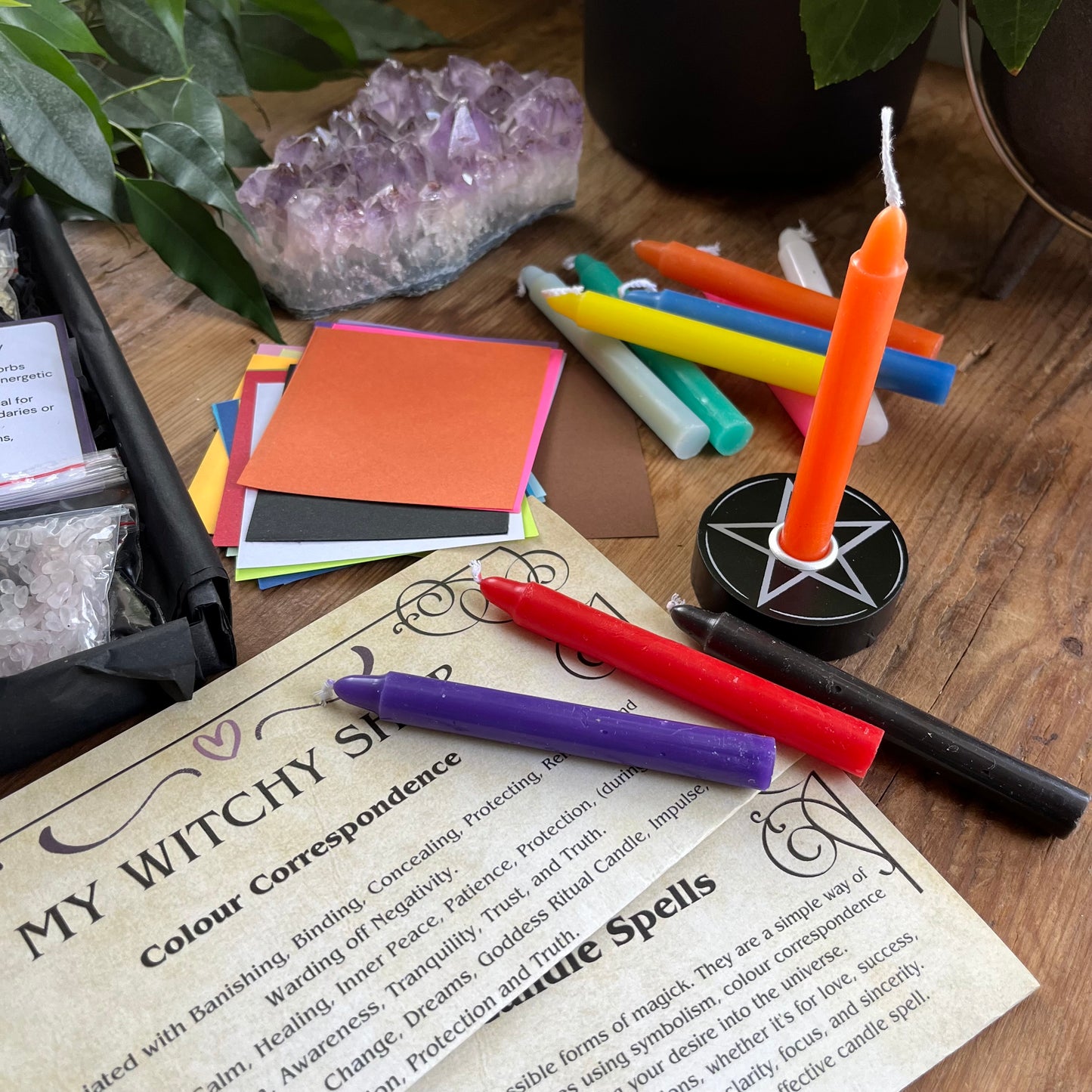 Colorful spell candles, candle spell holder and correspondence guide on a wooden surface with crystals