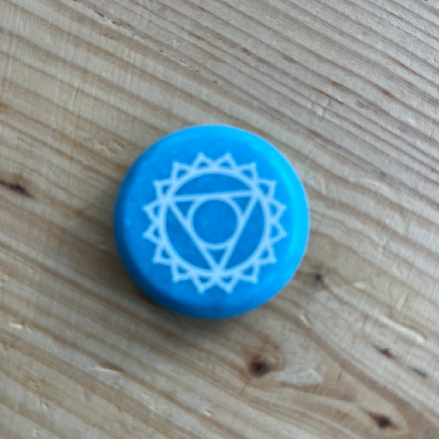 Blue flat circular meditation stone is engraved with the Throat Chakra symbol