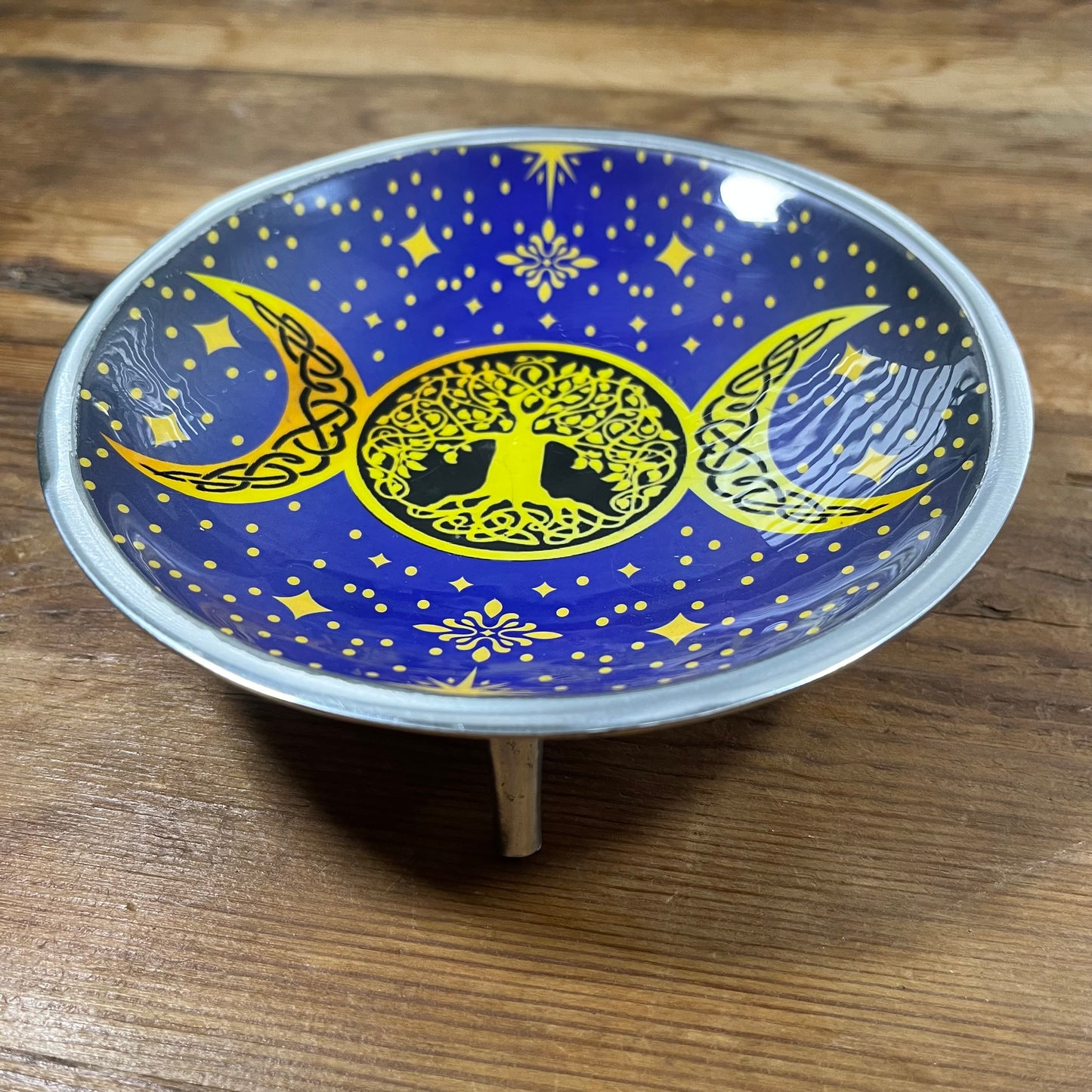 Decorative plate with yellow tree of life and moon designs on a blue background, placed on a wooden surface.