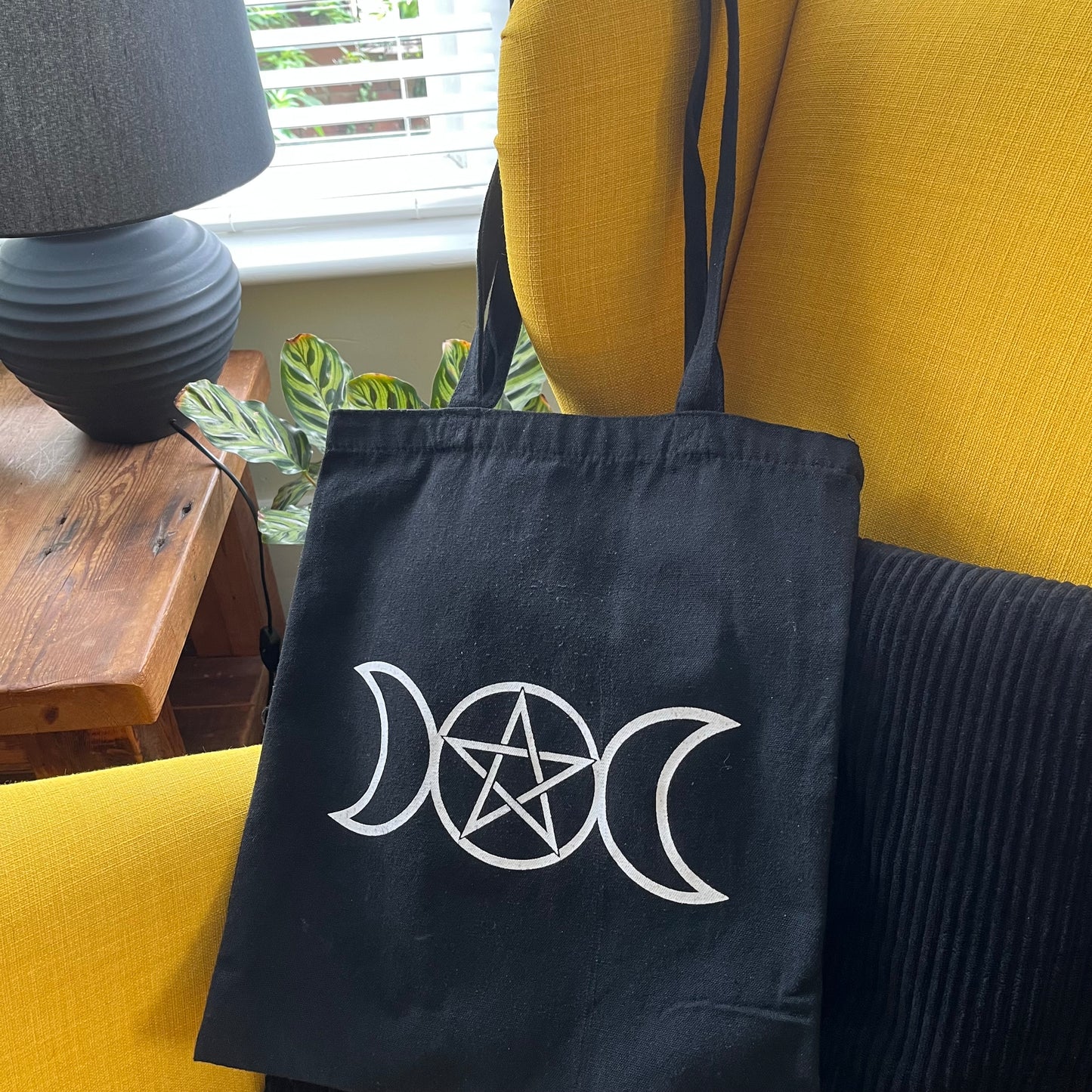 Black tote bag with white symbol on a yellow couch