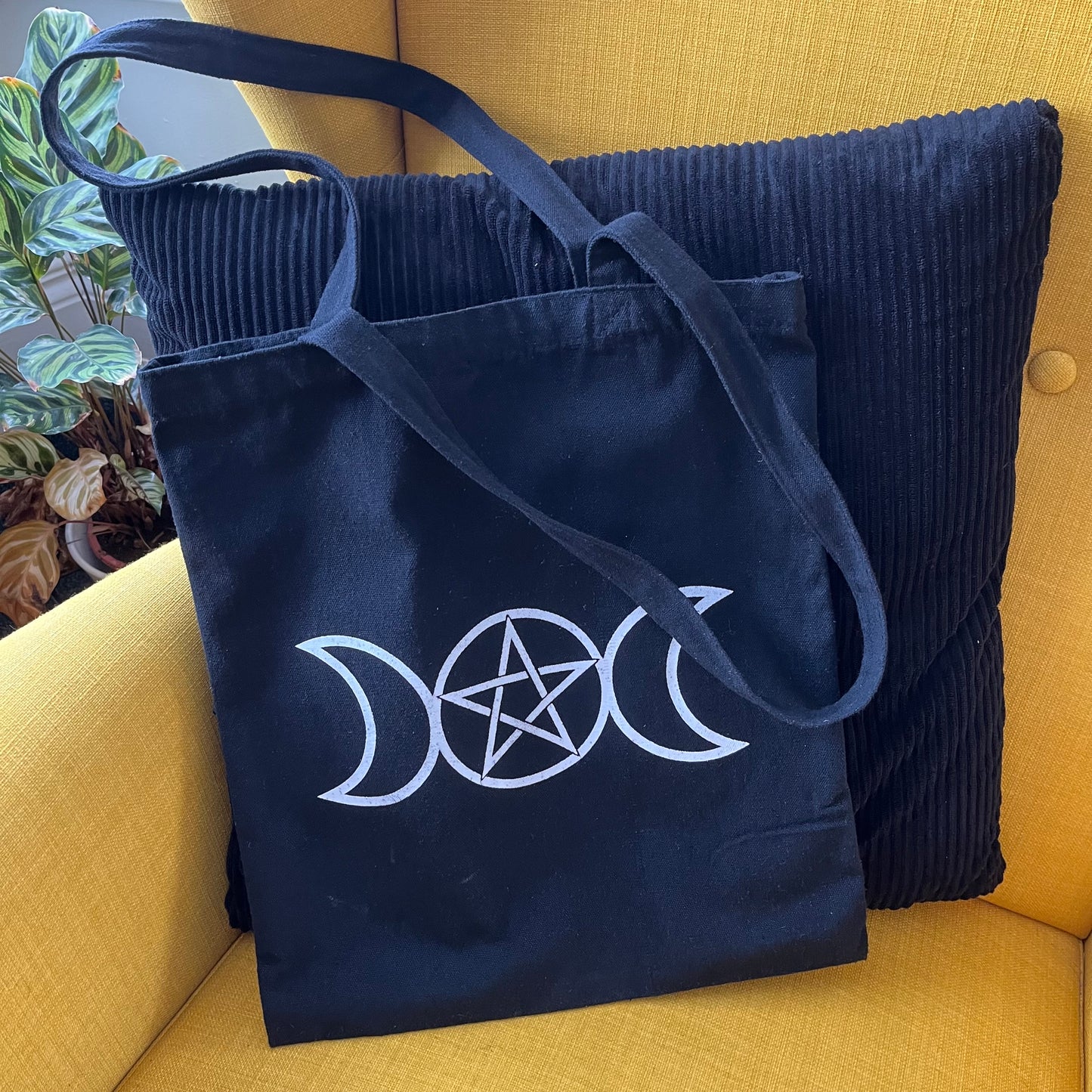 Black bag with white triple moon and pentagram symbol on a yellow couch