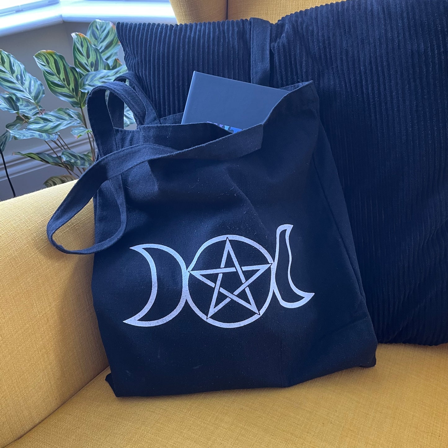 Black bag with white triple moon and pentagram symbol on a yellow couch