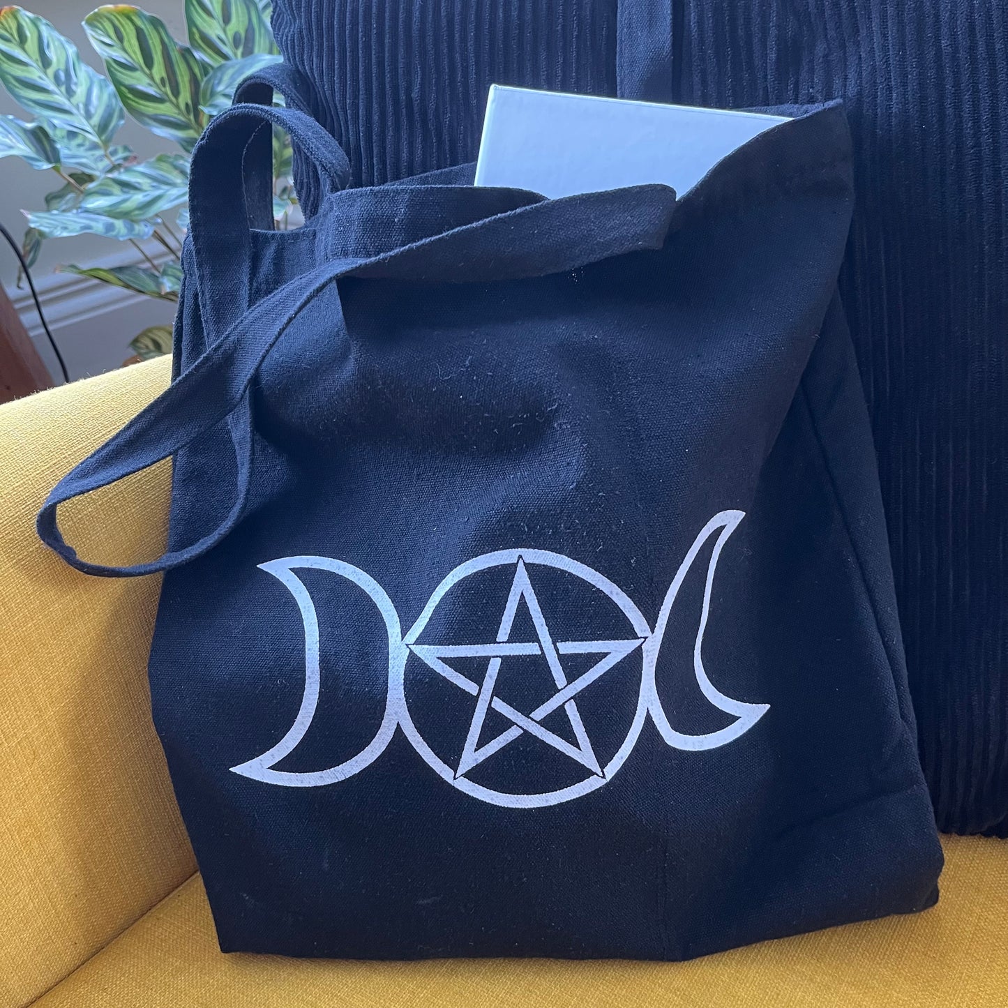 Black bag with white triple moon and pentagram symbol on a yellow couch