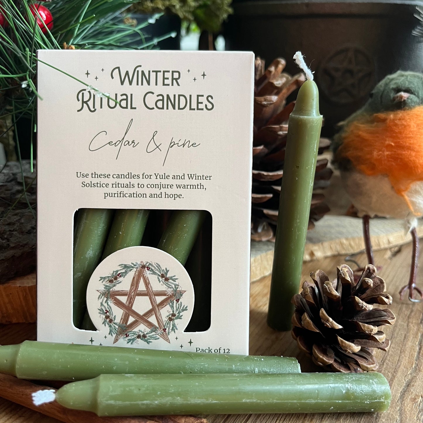 A set of 12 green spell cnadles in a cream coloured box adorned with a pentagram and a holly wreath.