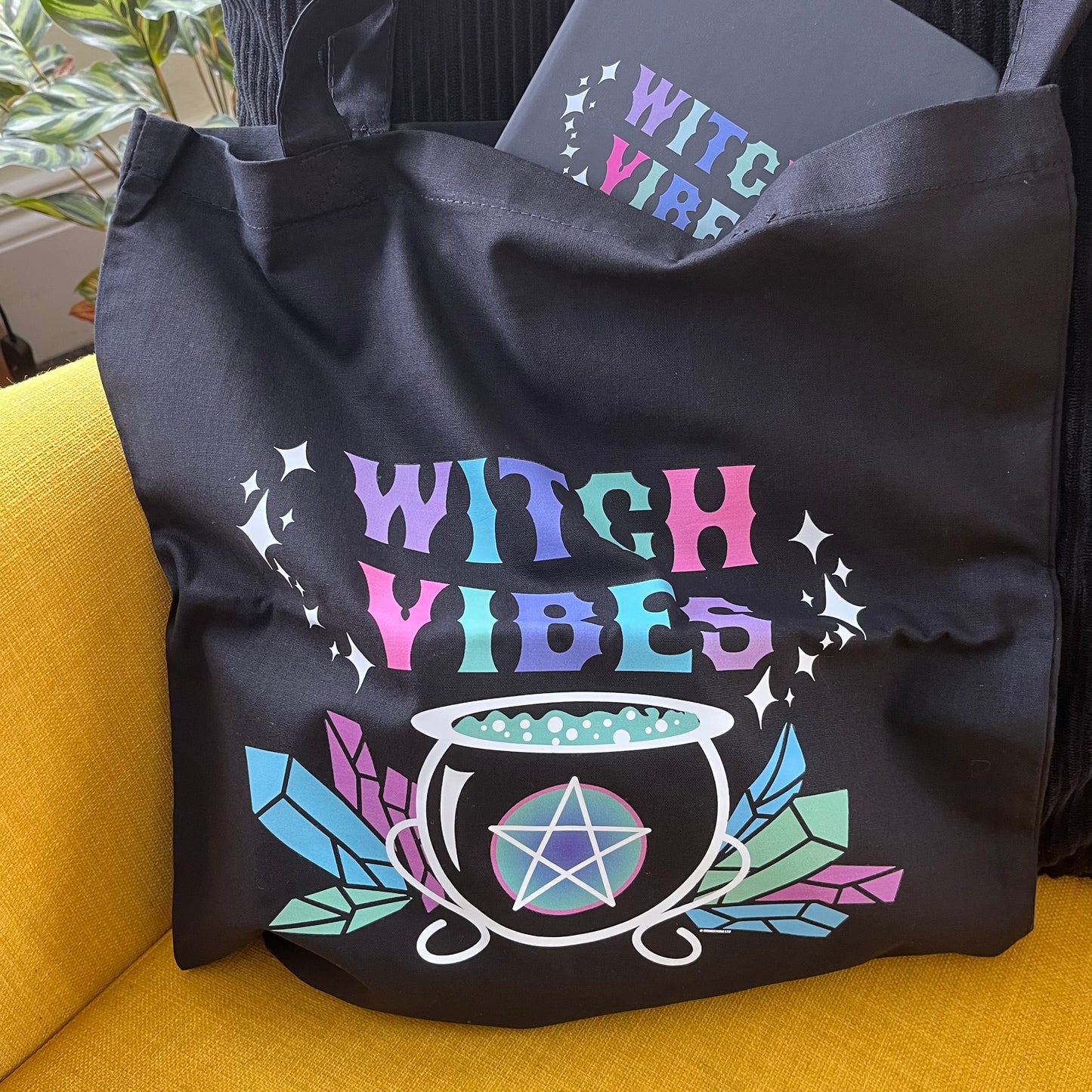 Black tote bag with 'Witch Vibes' design on a yellow couch