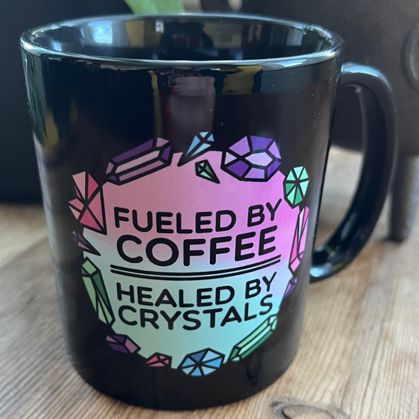 Black mug with colorful text and gemstone design on a wooden surface