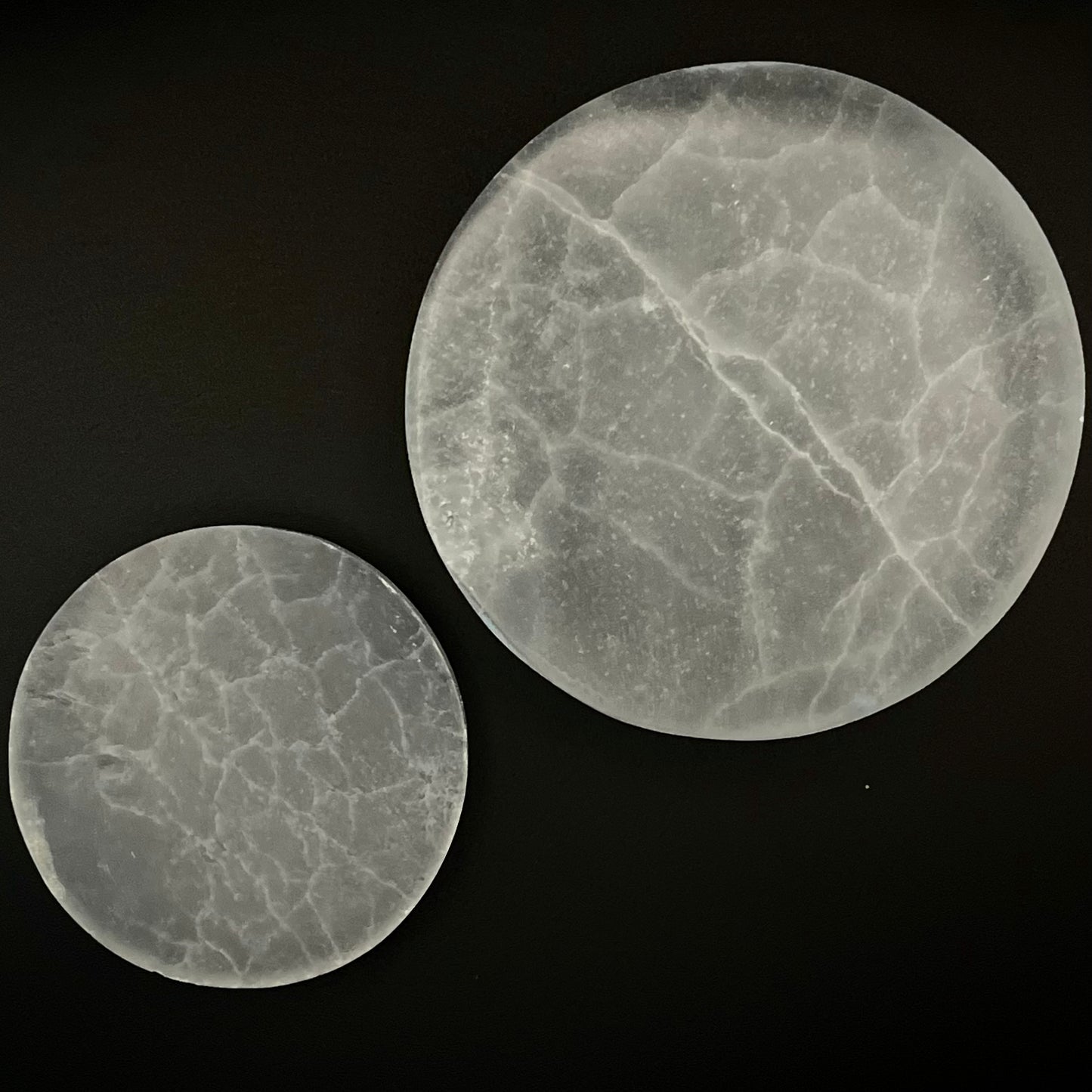 Two round translucent Selenite Crystal discs with natural crackle veining, displayed on a solid black background.