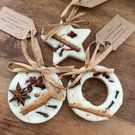 Decorative wax festive hanging decorations with star and circle shapes, tied with ribbons and containing spices on a wooden surface.