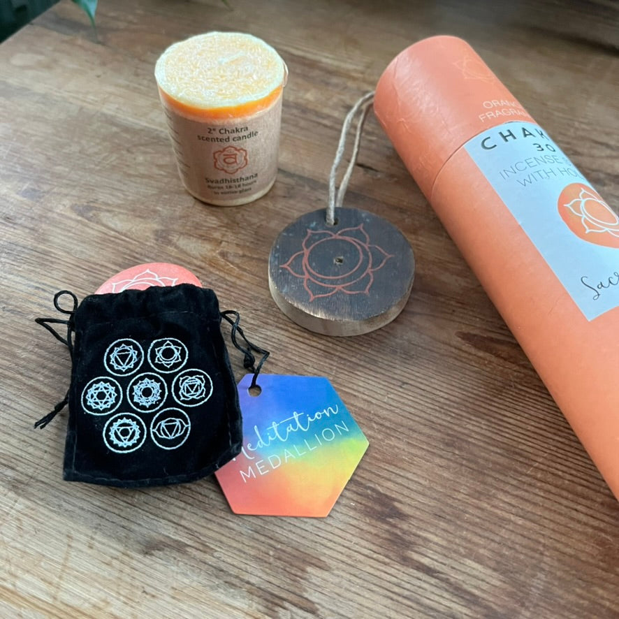Chakra-themed products including a candle, incense stick, and pouch on a wooden surface.