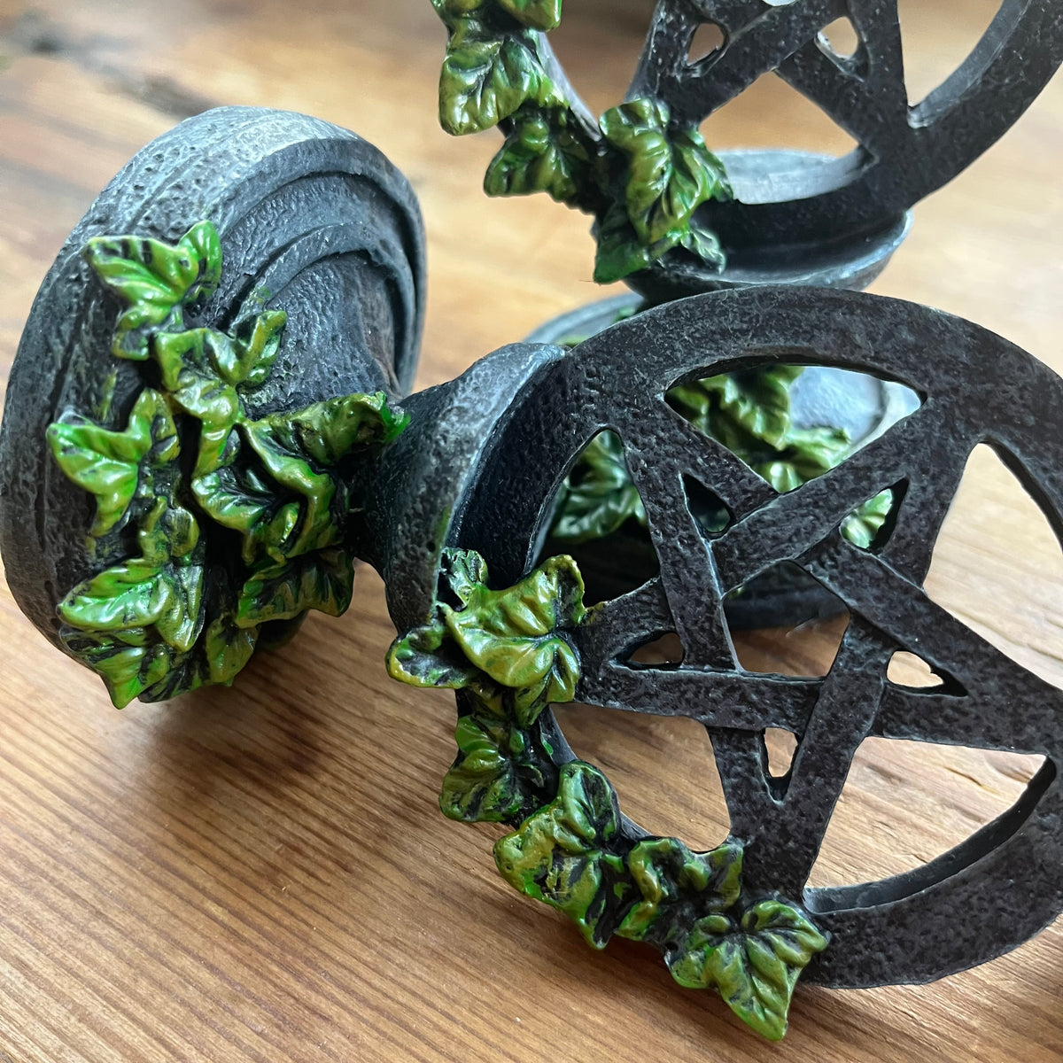 A close-up of a decorative candlestick holder featuring a pentagram design, accented with green leafy vines, shown on a wooden surface.